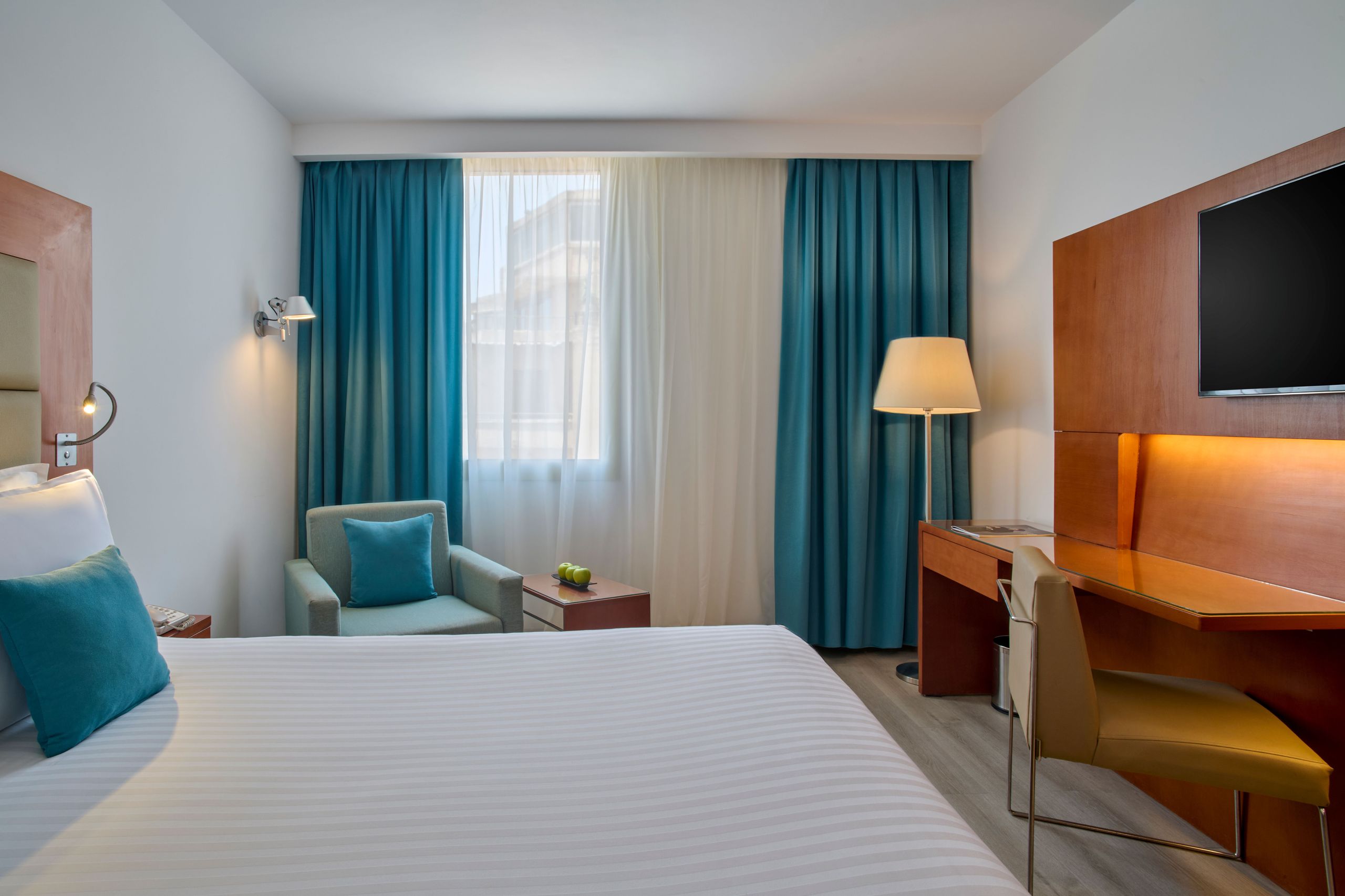 Une chambre d'hôtel moderne avec un lit, un fauteuil, un bureau, une chaise et une télévision à…