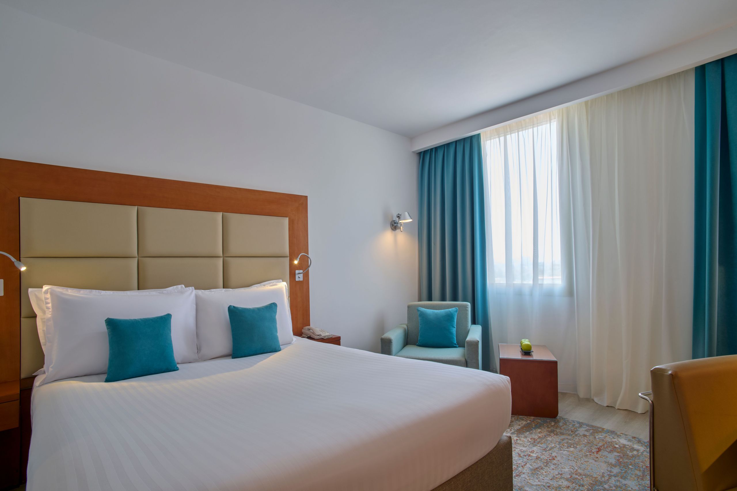 Une chambre d'hôtel propre et bien éclairée avec un lit, des oreillers, un fauteuil et des rideaux.