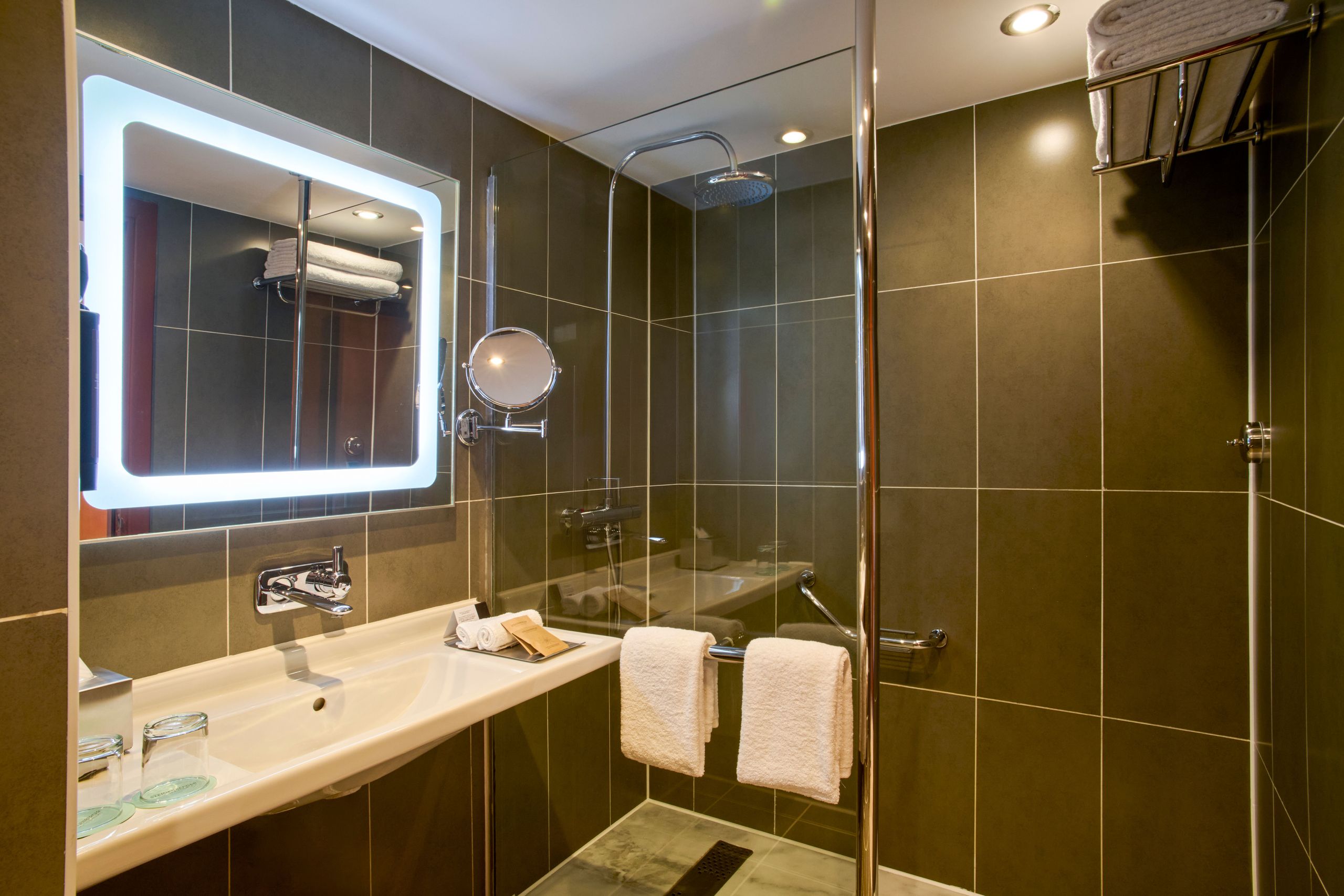 La photo montre une salle de bain moderne avec un lavabo, un miroir éclairé, une douche vitrée et…