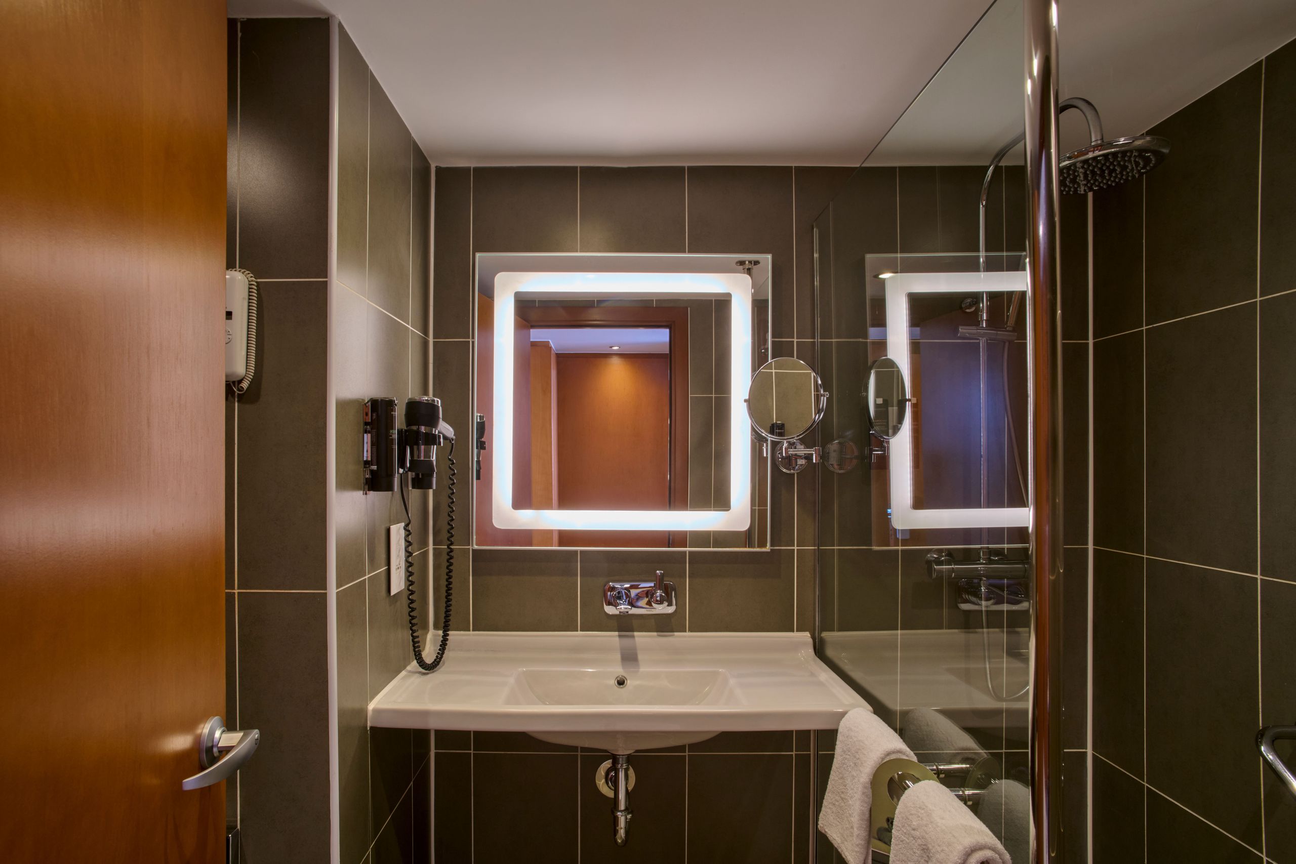 Une salle de bains moderne avec un lavabo, un miroir éclairé et une cabine de douche en verre.