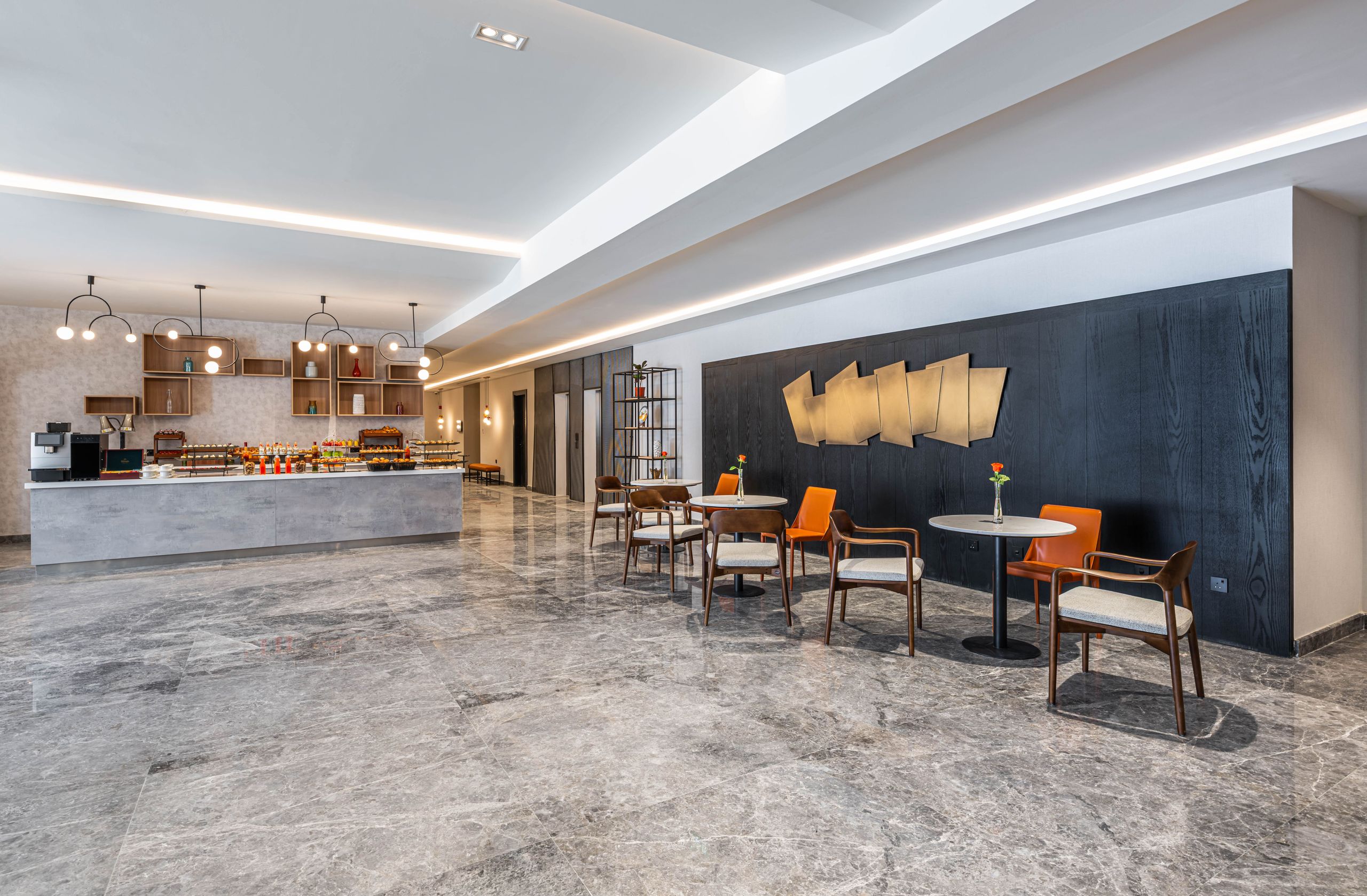 The photo shows a modern cafe or lounge area with tables and chairs, a counter with refreshments,…
