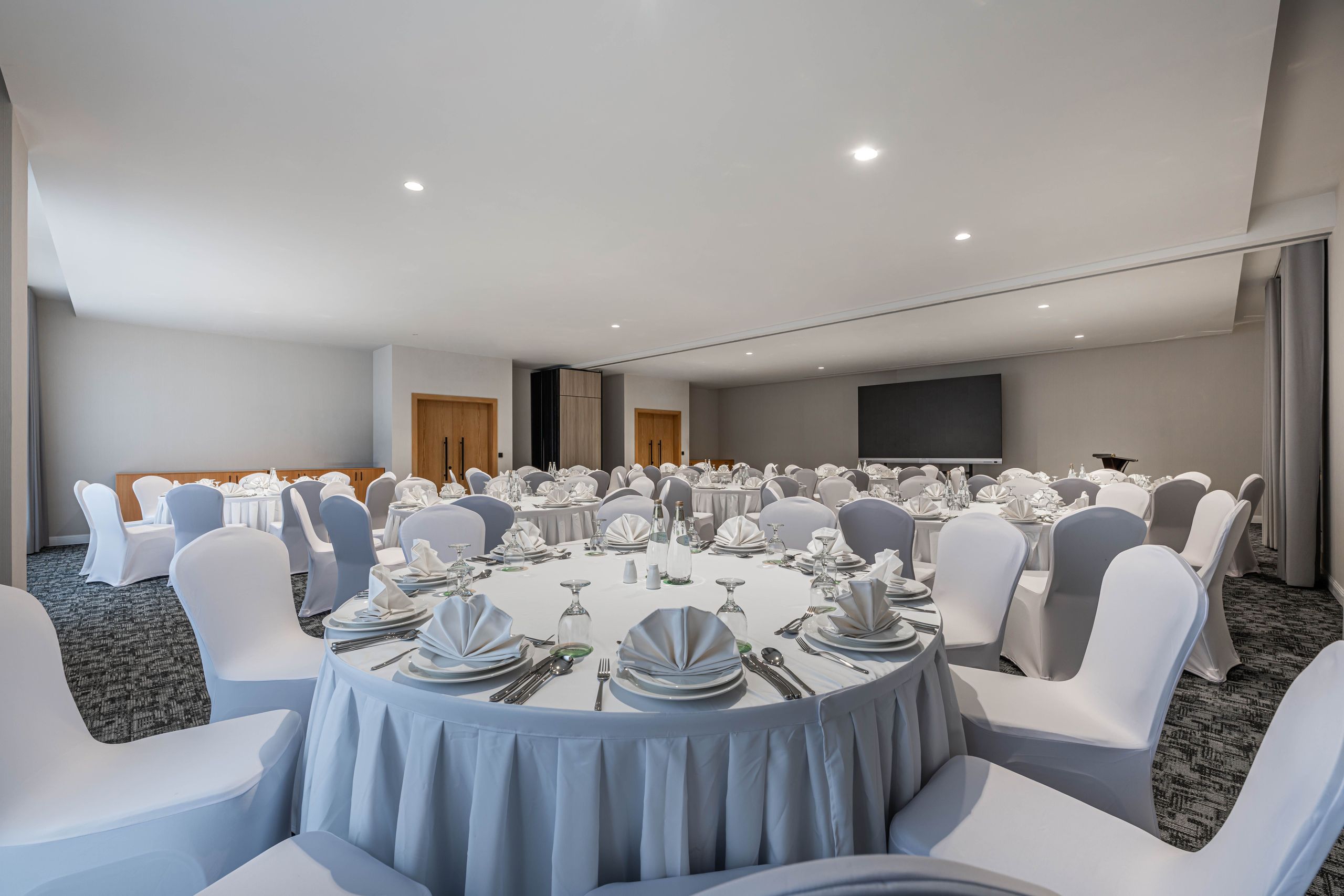 A banquet hall set up with round tables and chairs covered in white cloth, arranged for a formal…