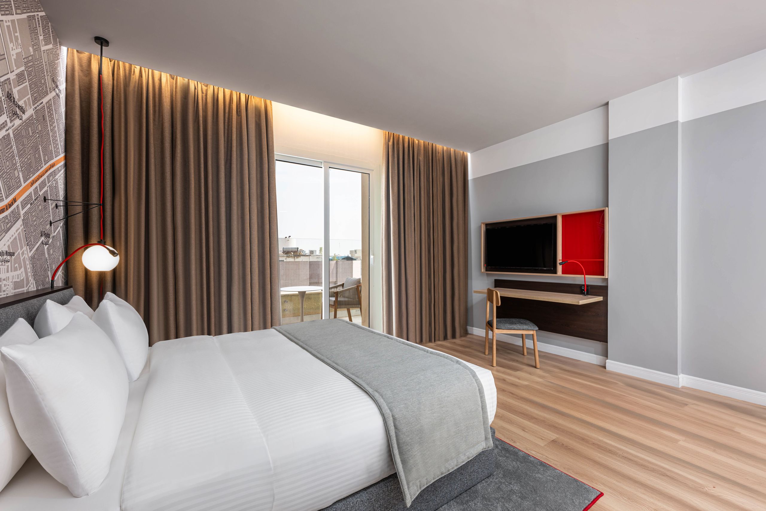 Een moderne hotelkamer met een groot bed, een nachtlampje, gordijnen die een schuifdeur van glas…
