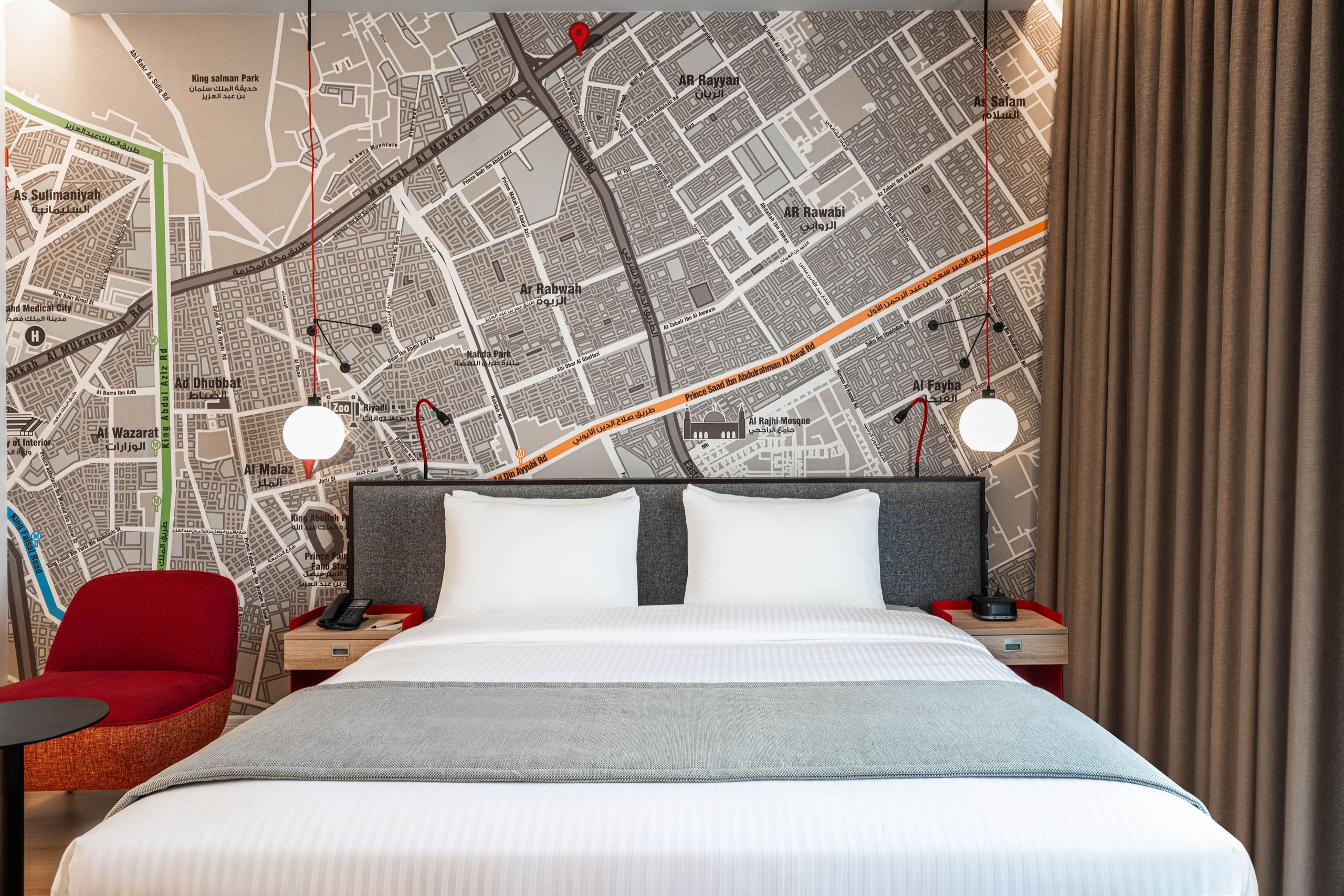 De foto toont een moderne slaapkamer met een groot bed in het midden, een muur met een kaart…