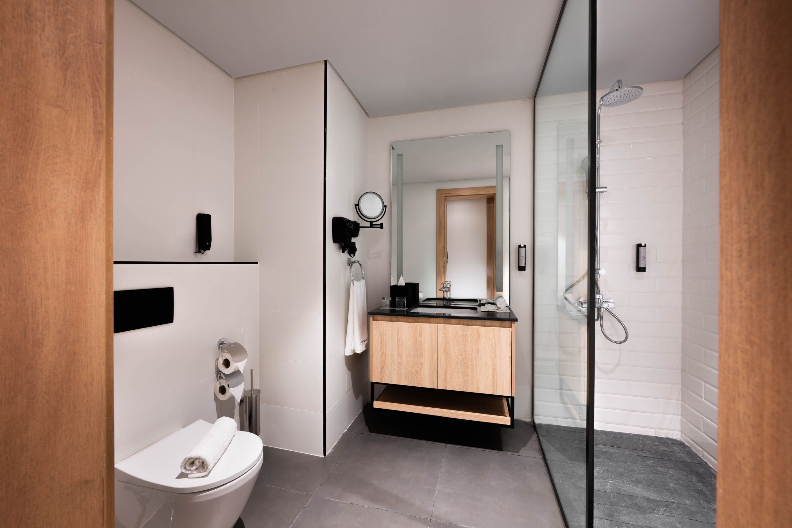 Een moderne badkamer met een toilet, wastafel, spiegel en een inloopdouche met glazen afscheiding.