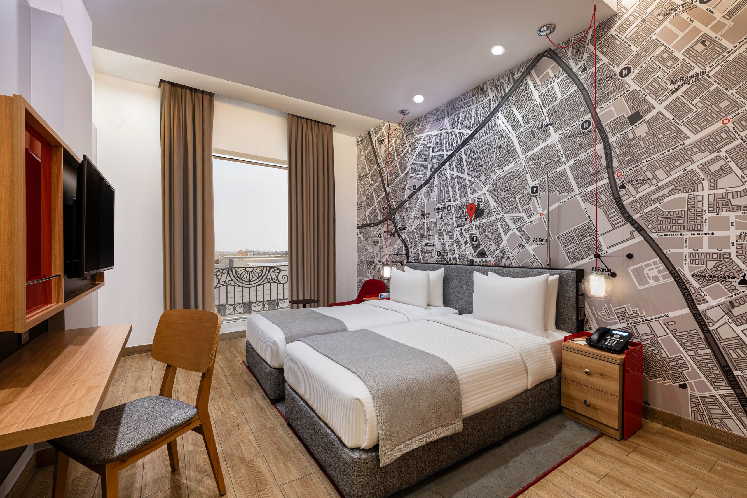 Ett modernt hotellrum med två enkelsängar, ett skrivbord, en stol, en väggmonterad tv och en stor…