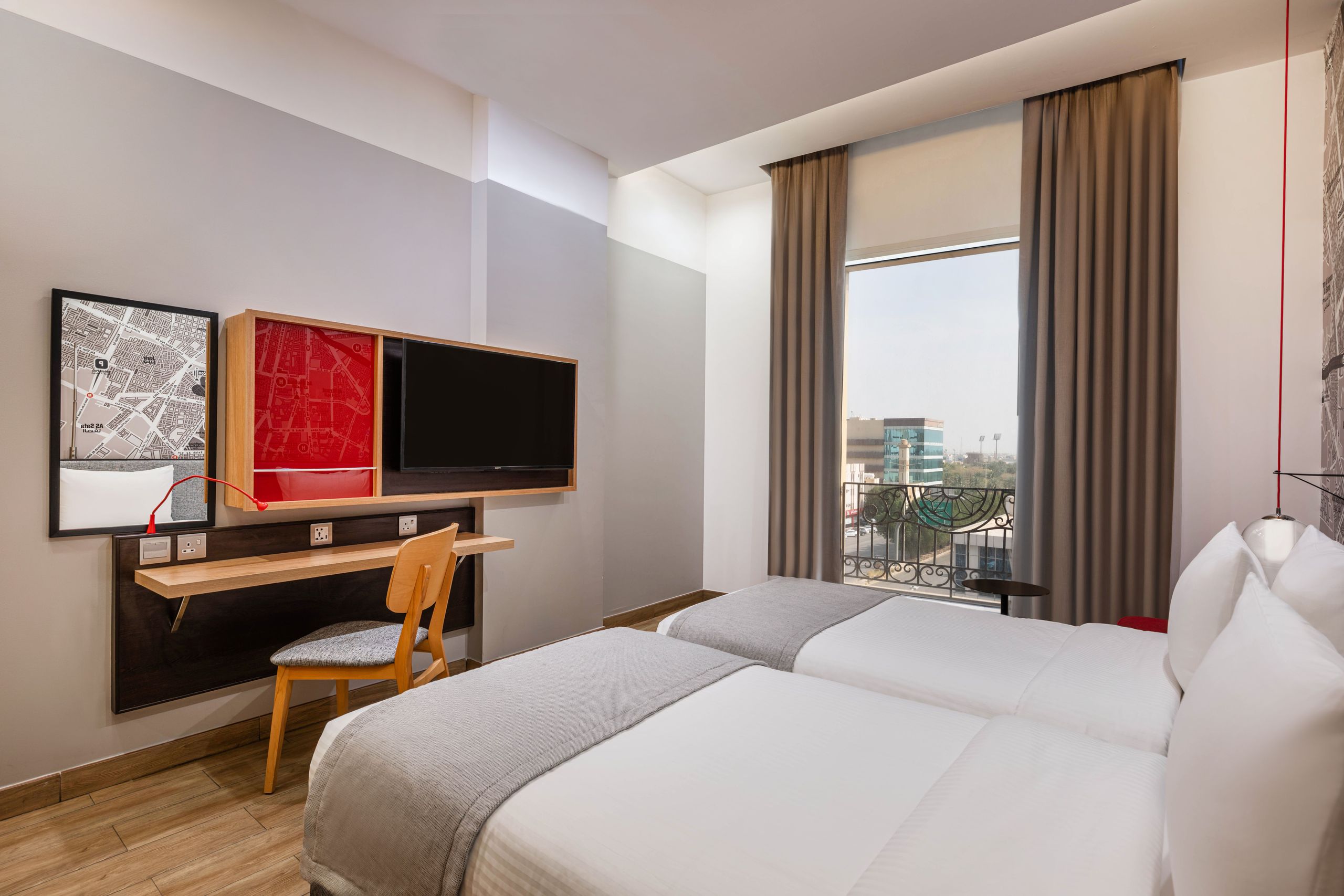 Ett modernt hotellrum med två enkelsängar, ett skrivbord med stol, en väggmonterad TV och ett…