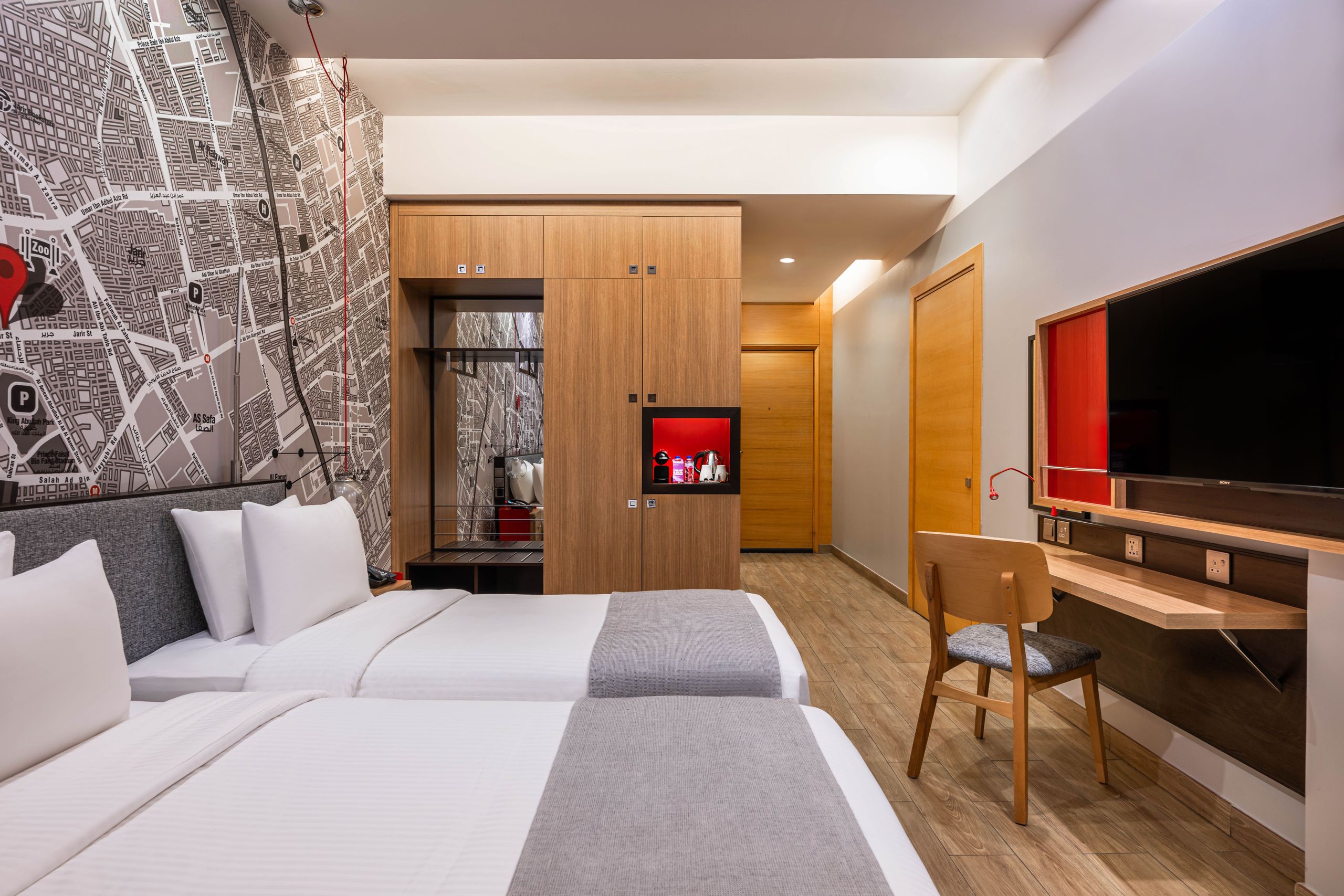 Ett modernt hotellrum med två enkelsängar, en trägarderob, ett skrivbord med stol och en…