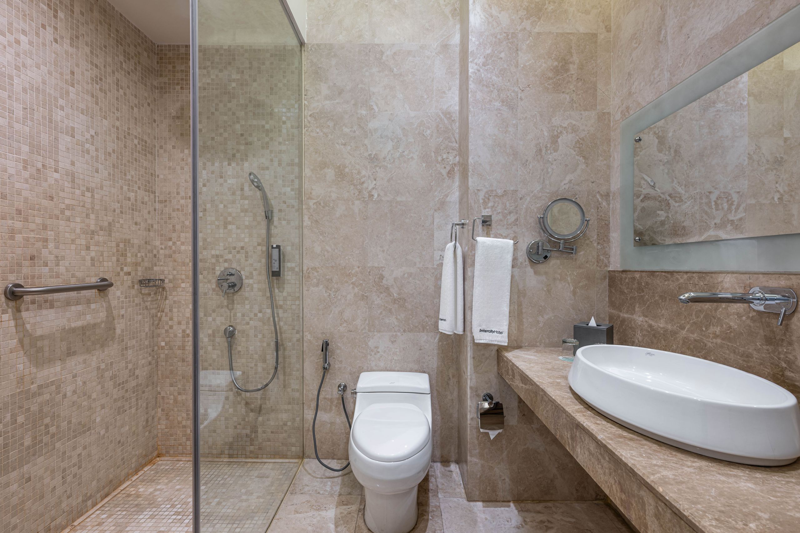 Ett modernt badrum med en glasinklädd dusch, en toalett och en bänk med handfat och spegel.