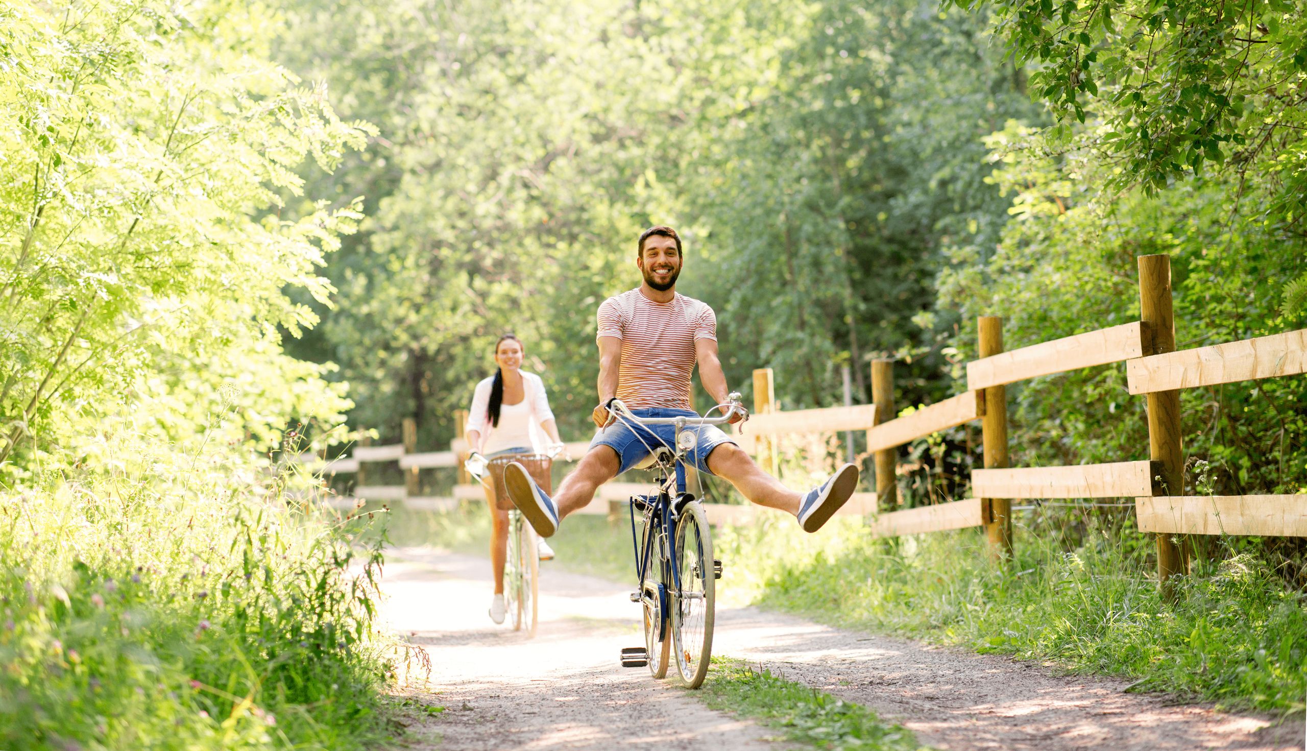 Ein Mann und eine Frau fahren auf einem von Wald umgebenen Weg Fahrrad.