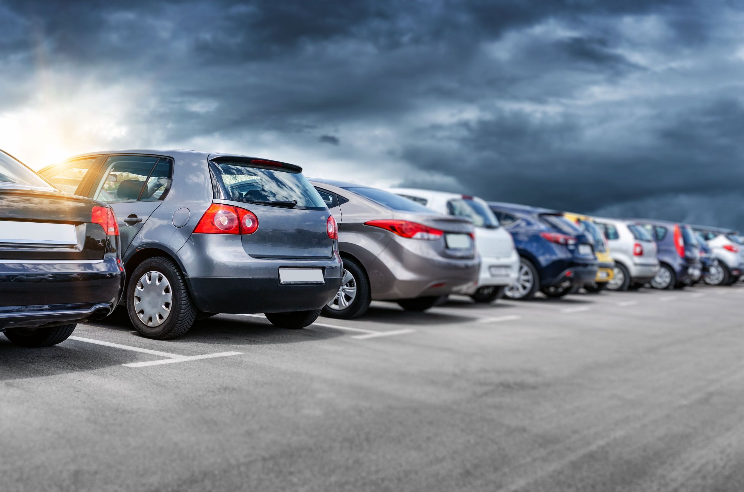 A row of parked cars in an outdoor parking lot under a cloudy sky.