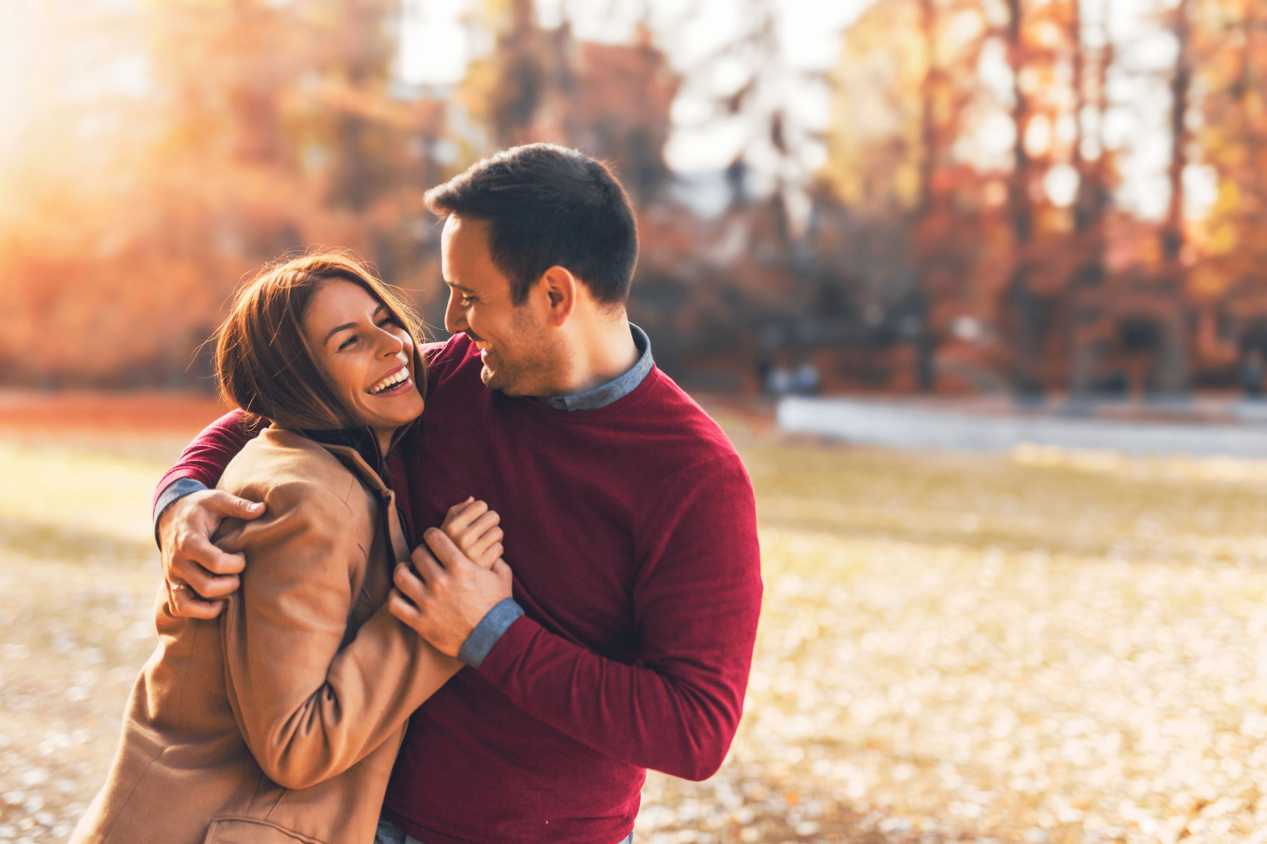 A couple is happily embracing outdoors in an autumn setting.