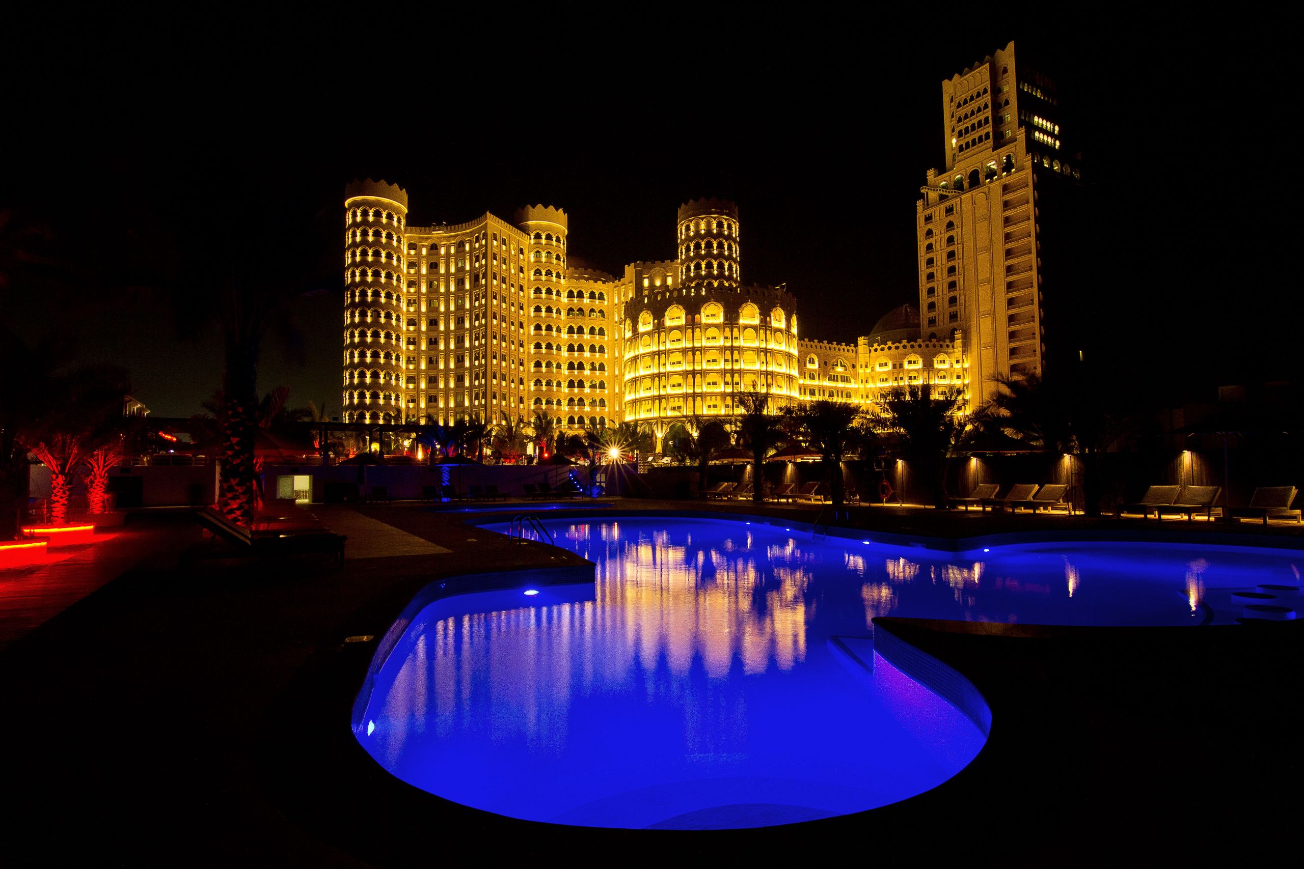 A night view of a well-lit building with a swimming pool in the foreground.
