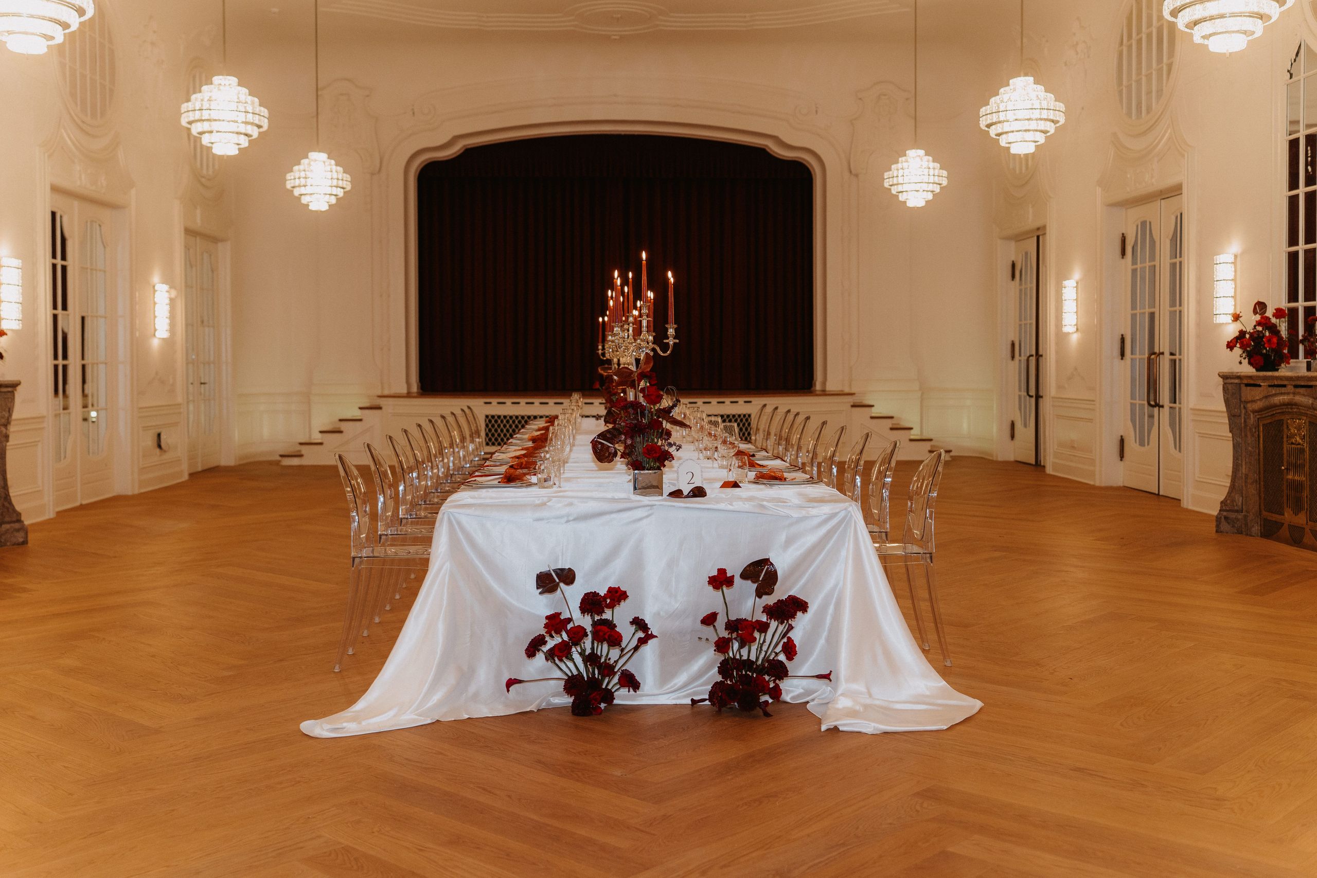 Formálně prostřený jídelní stůl v elegantní místnosti s lustry a dřevěnou podlahou.