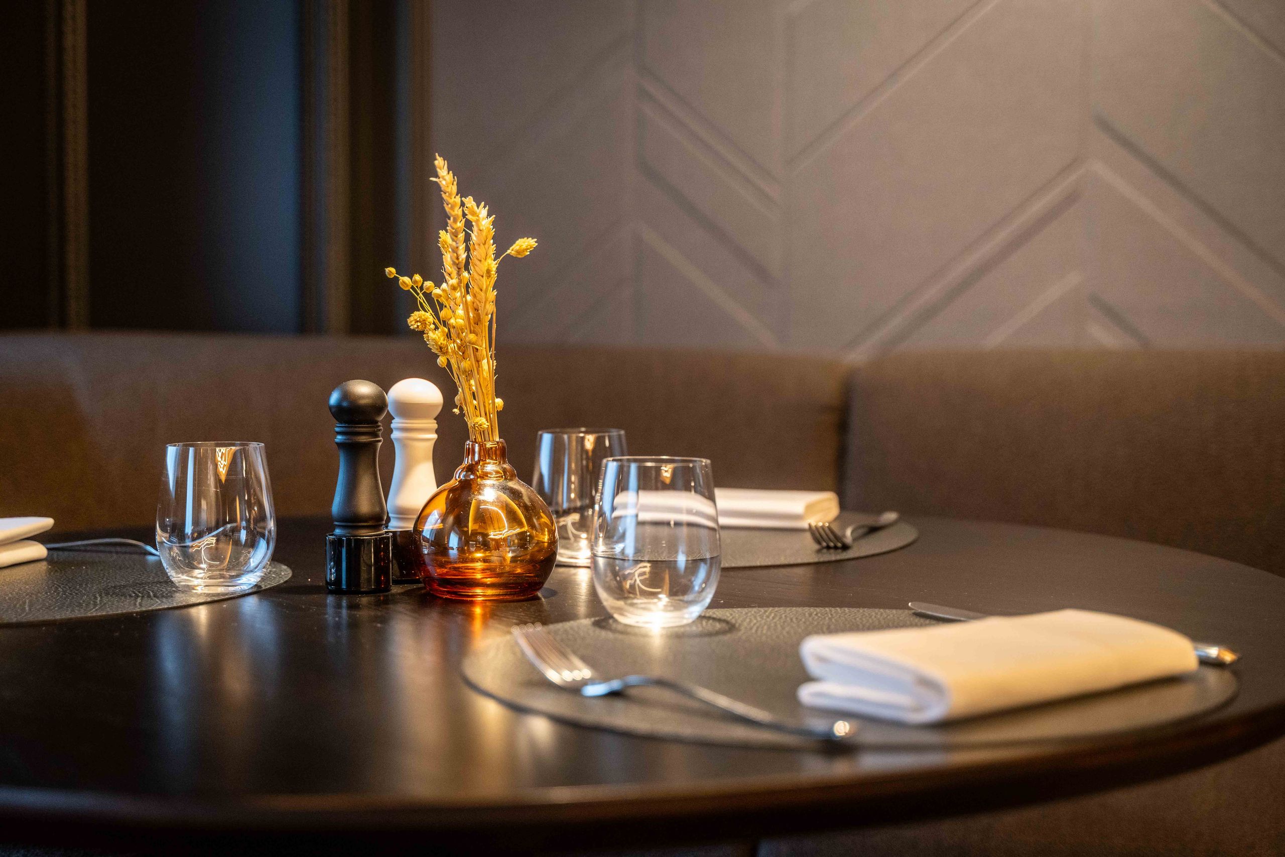 Une table à manger ronde dressée avec des verres, des couverts, des serviettes, un petit vase avec…