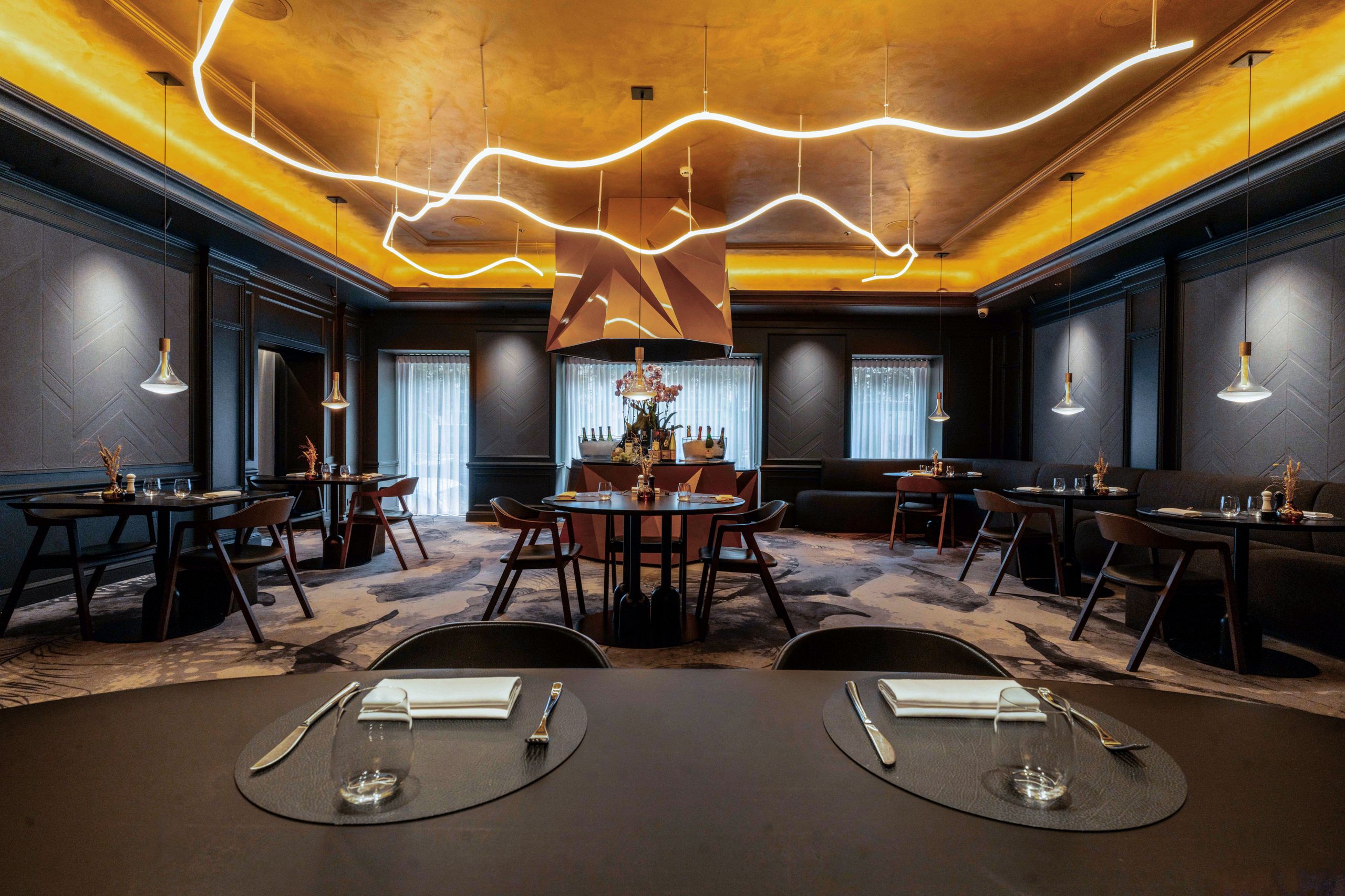 A foto mostra o interior de um restaurante moderno e elegante com mesas arrumadas e luminárias…