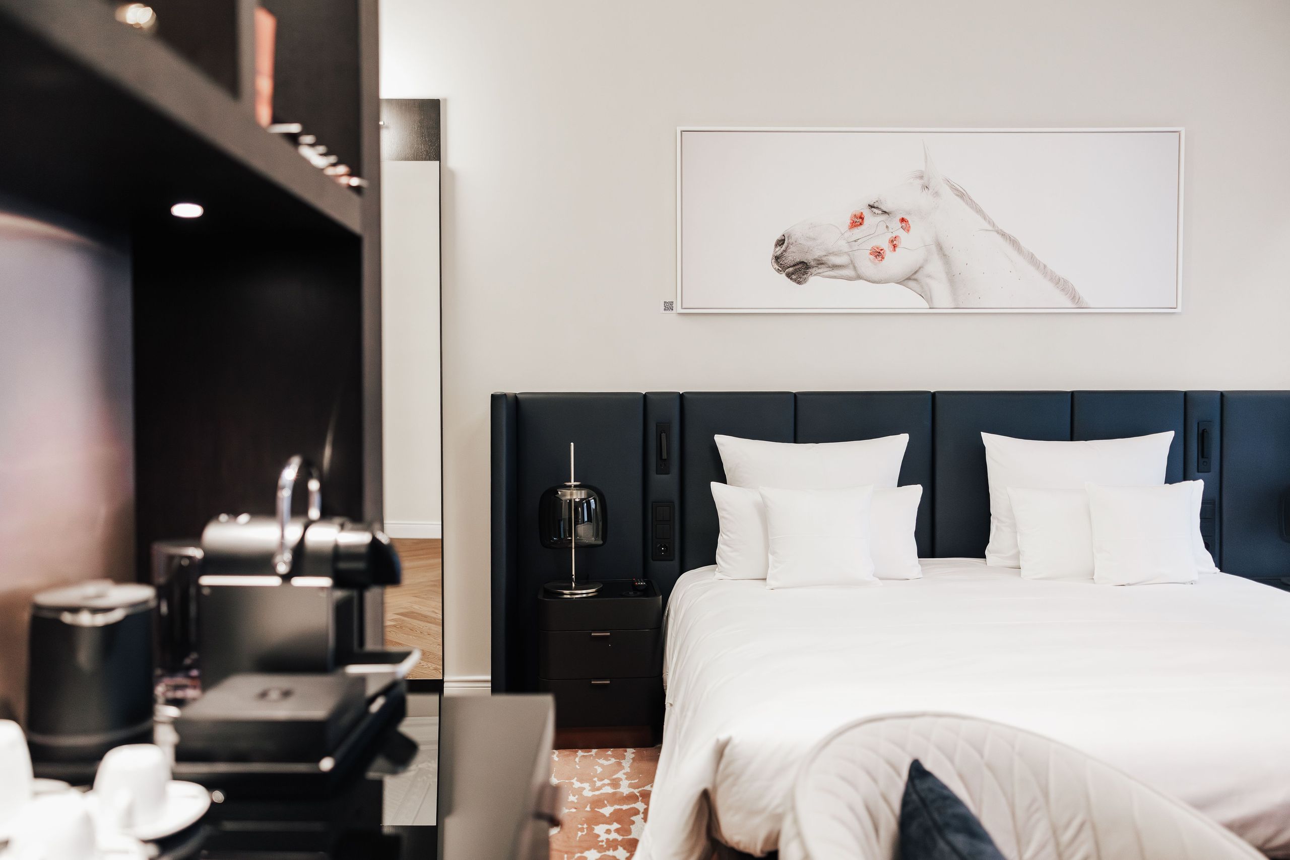 La foto mostra una camera d'hotel moderna con un grande letto, comodini, una macchina del caffè e…