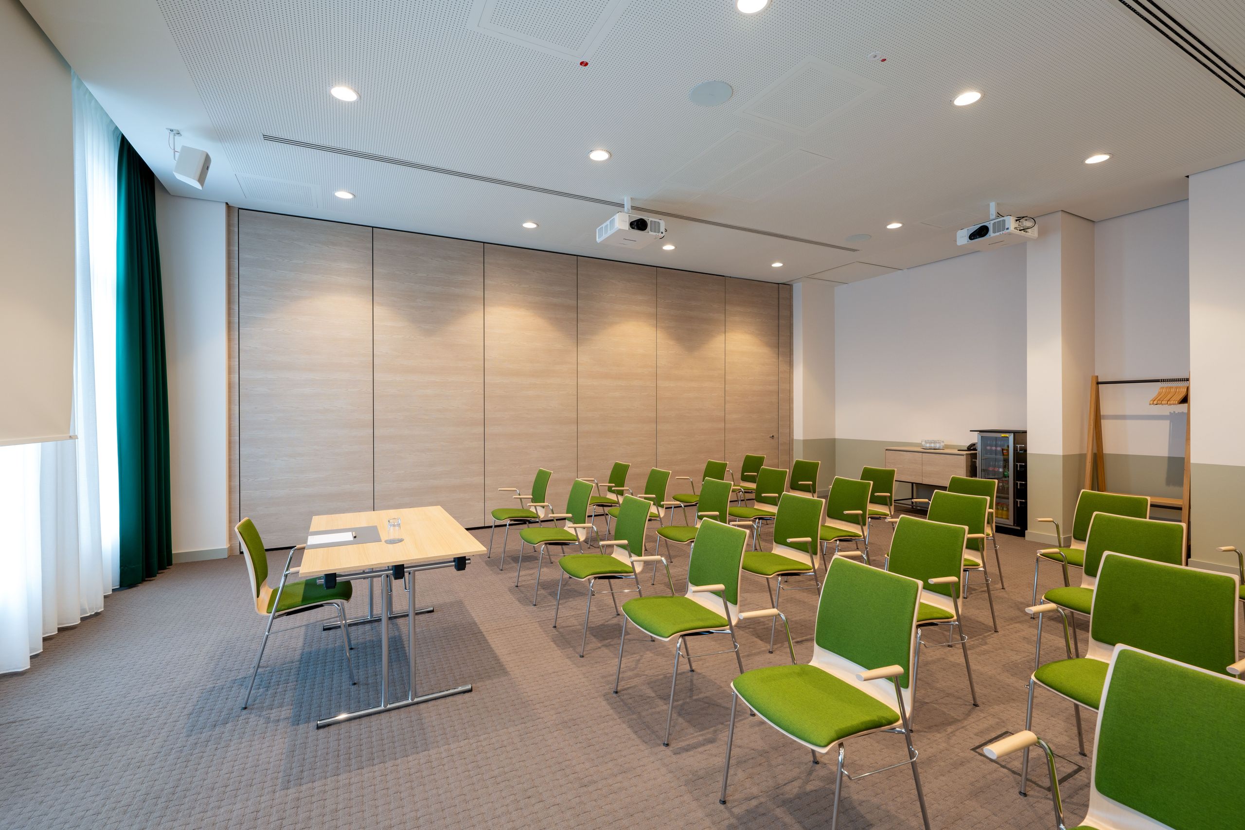 A modern conference or meeting room with rows of green chairs facing a speaker's table at the front.