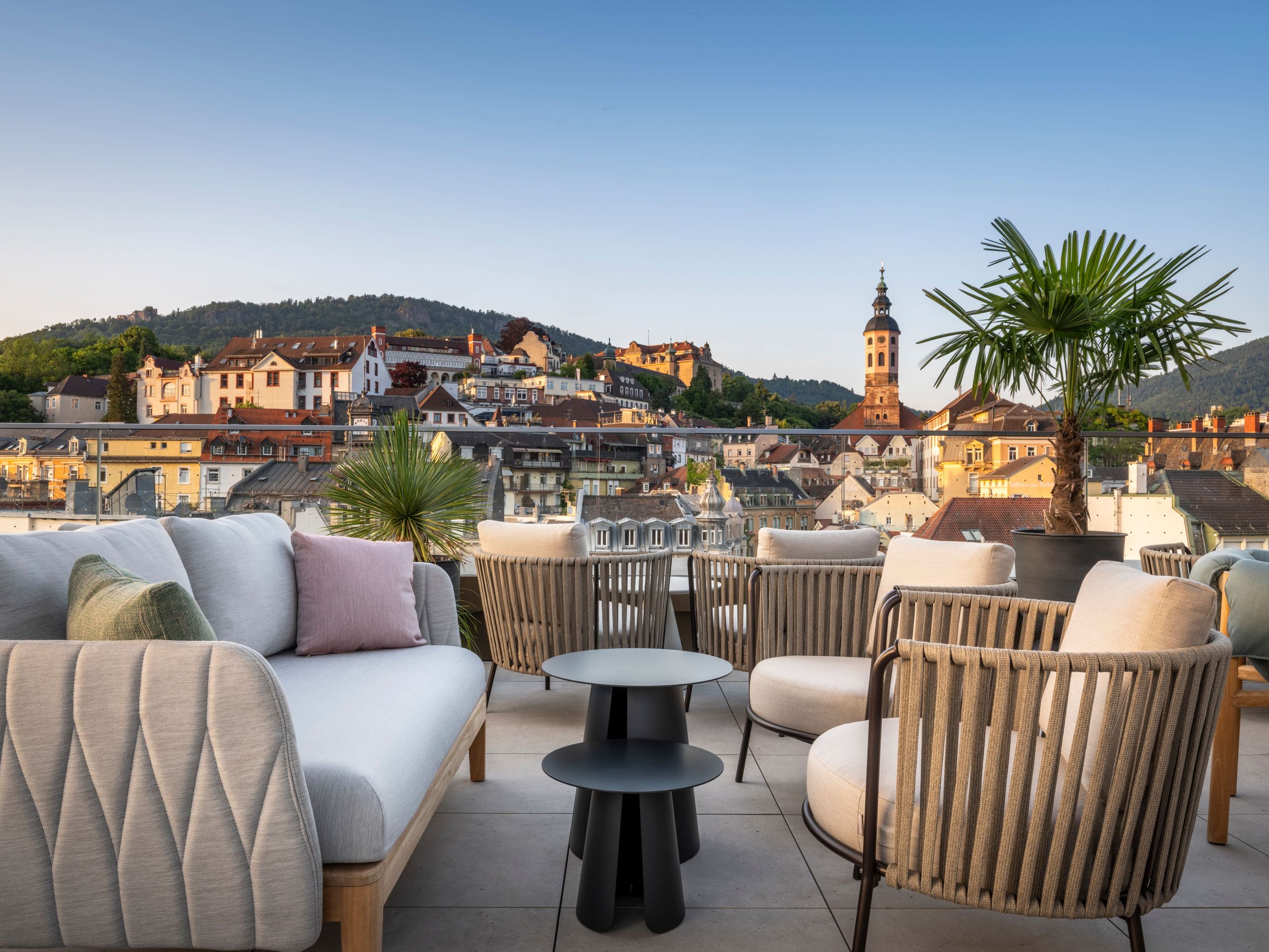 Eine Dachterrasse mit moderner Außenmöbel, die auf eine Stadt mit historischen Gebäuden und einen…