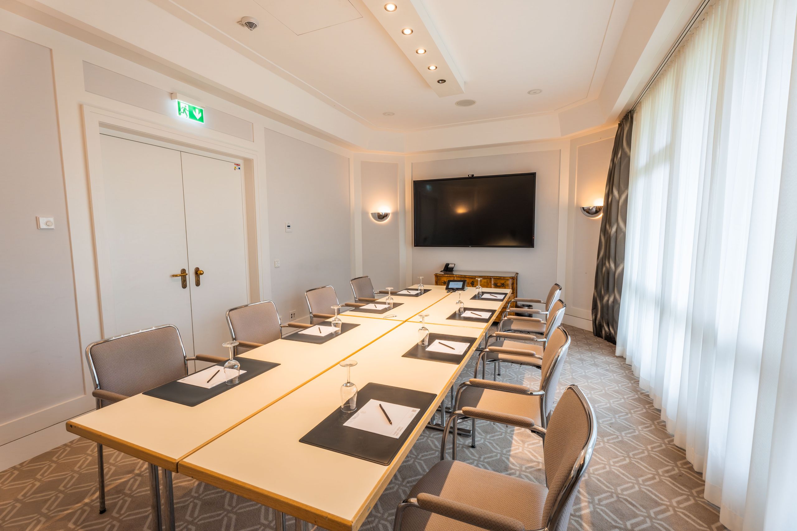 Ein Konferenzraum mit einem langen Besprechungstisch, Stühlen, Notizblöcken und einem großen…
