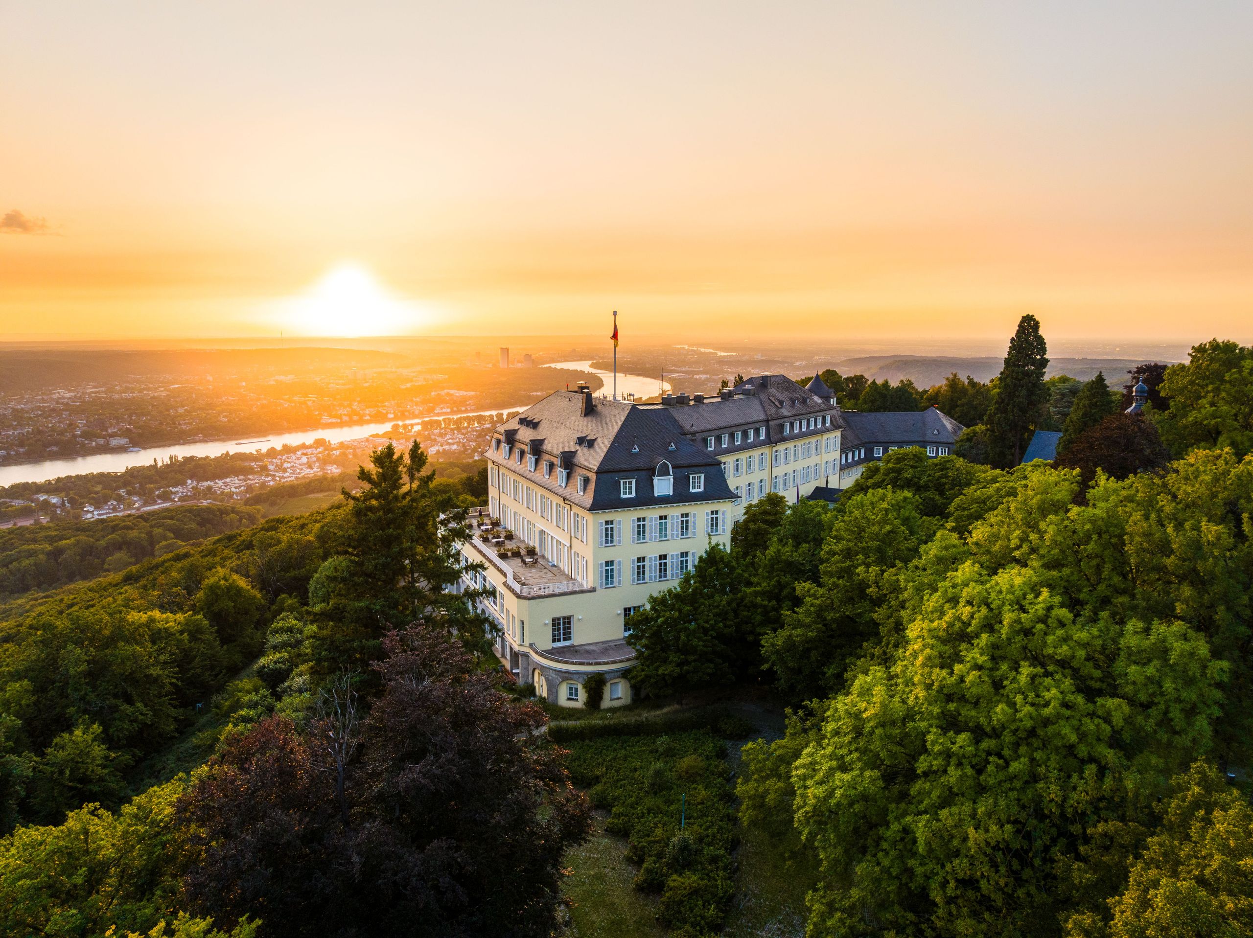 Ein großes Gebäude, umgeben von Bäumen, mit Blick auf eine Stadt bei Sonnenuntergang.