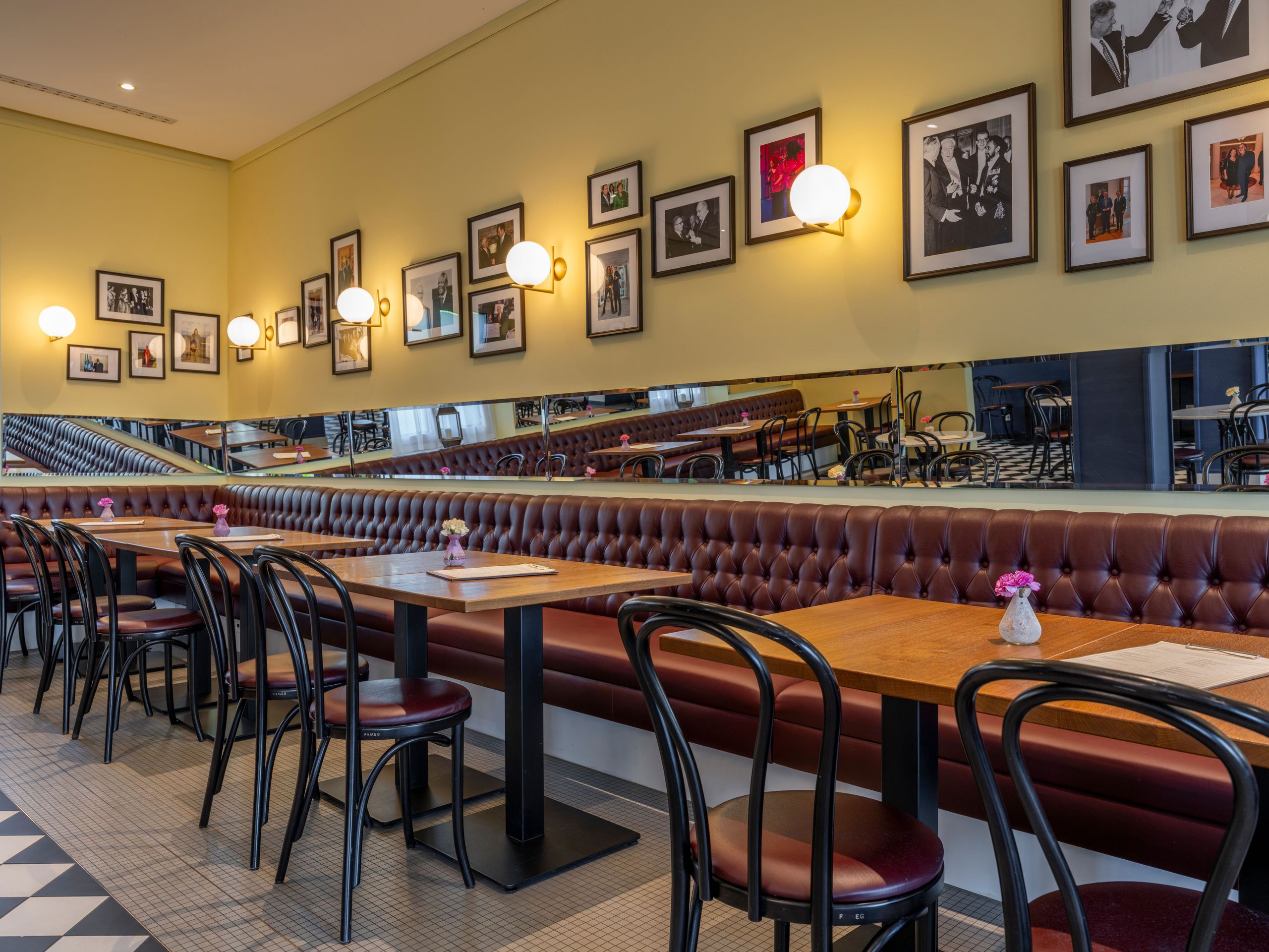 Das Foto zeigt das Innere eines Restaurants oder Cafés mit Holztischen, Stühlen, einer langen…