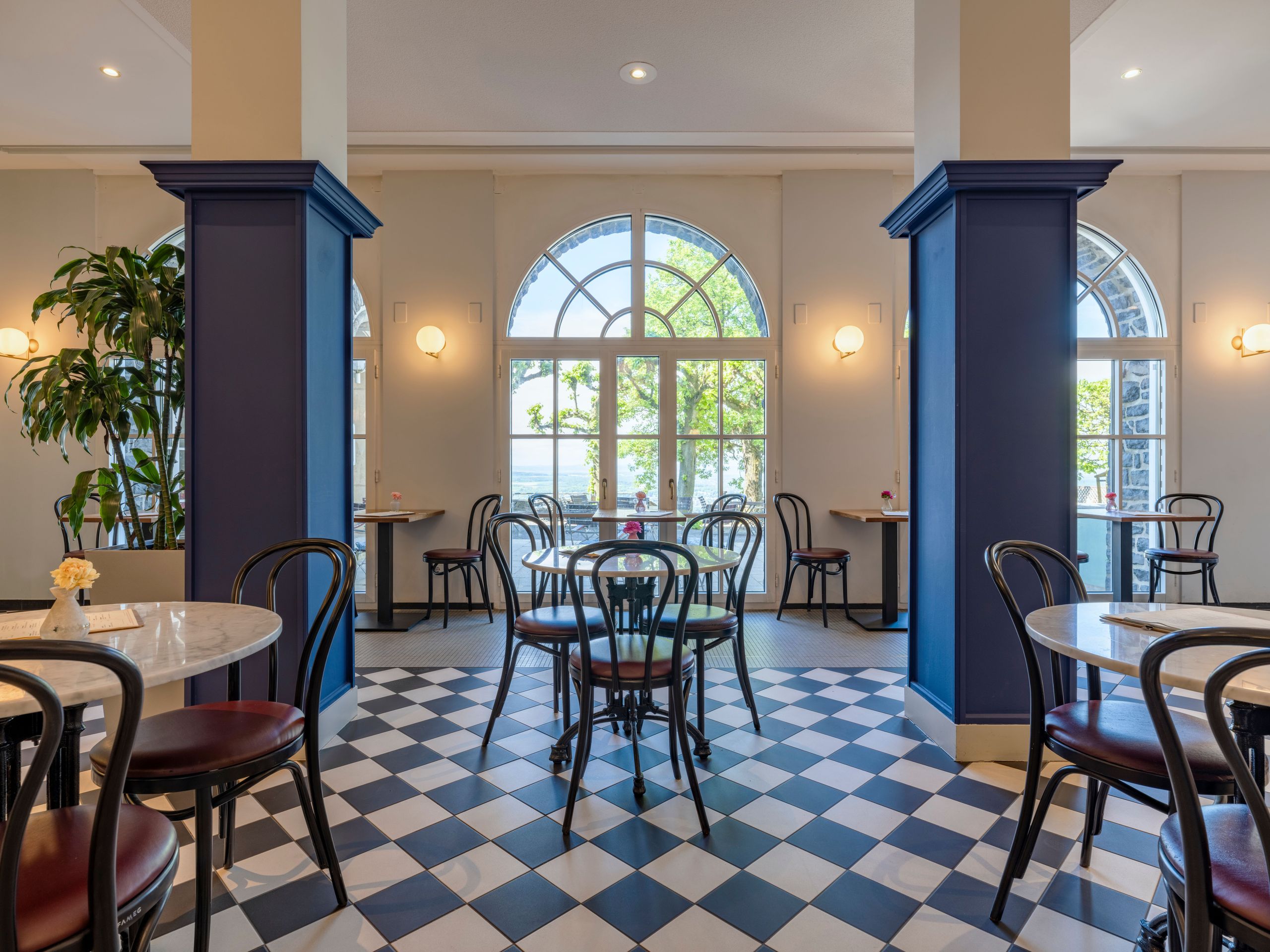 The photo shows a well-lit cafe or restaurant interior with tables, chairs, large windows, and…
