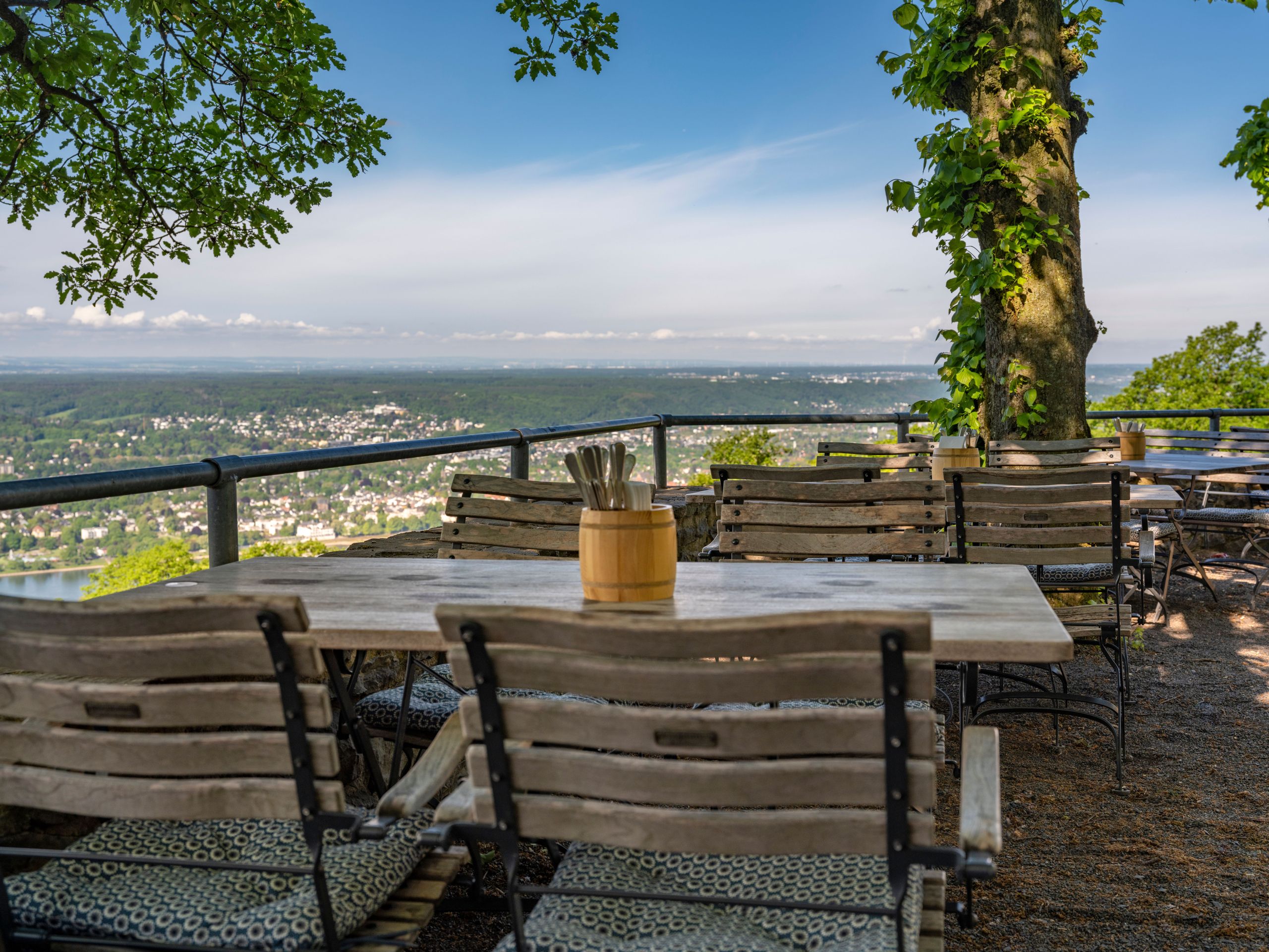 Ein Außenbereich mit Holztischen und Stühlen mit Blick auf eine malerische Stadt und einen Fluss.