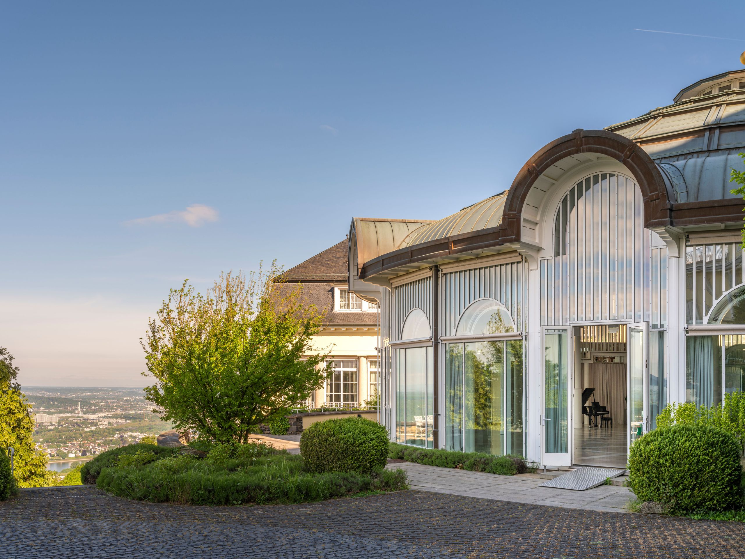 Ein großes Glasgewächshaus-ähnliches Gebäude mit Blick auf eine Stadtsilhouette im Hintergrund.