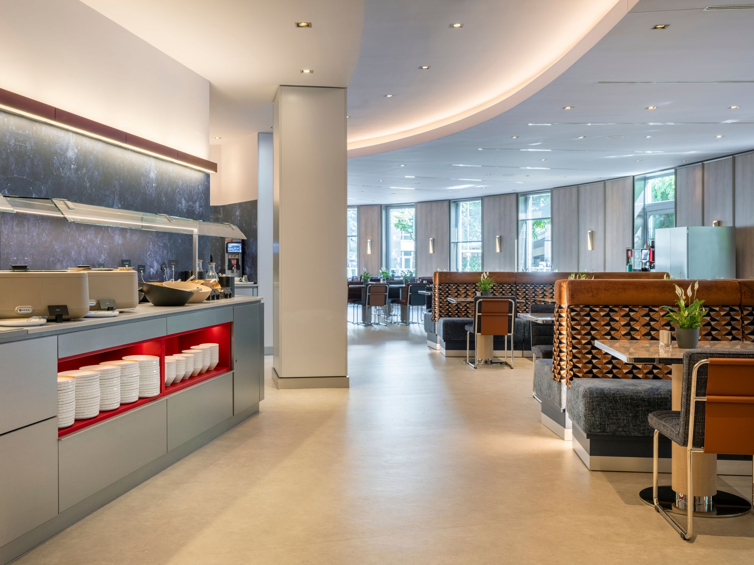 A modern and clean cafeteria or dining area with booths and tables, featuring a buffet counter on…