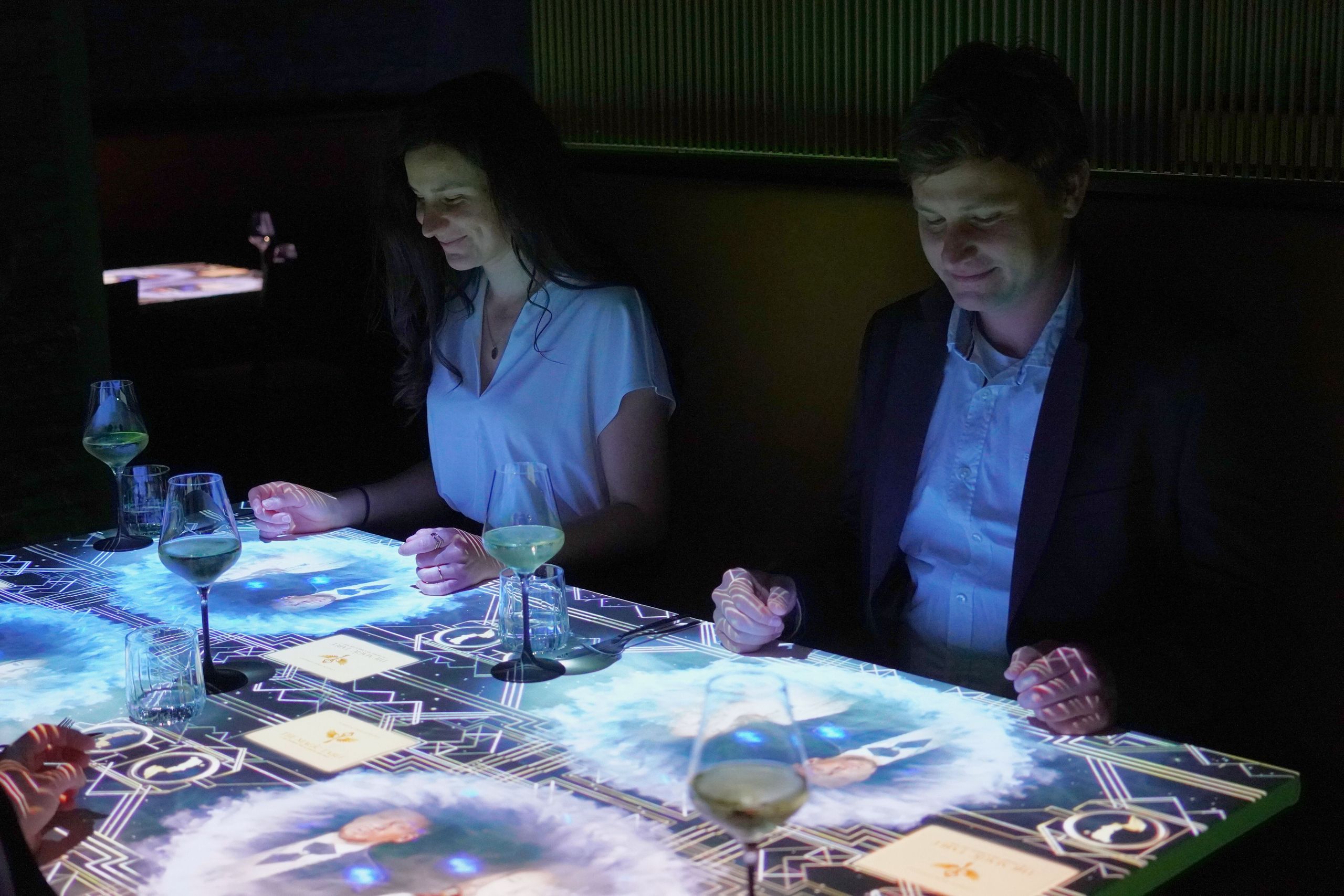 Zwei Personen sitzen an einem Tisch und interagieren mit einer beleuchteten, digitalen Oberfläche.