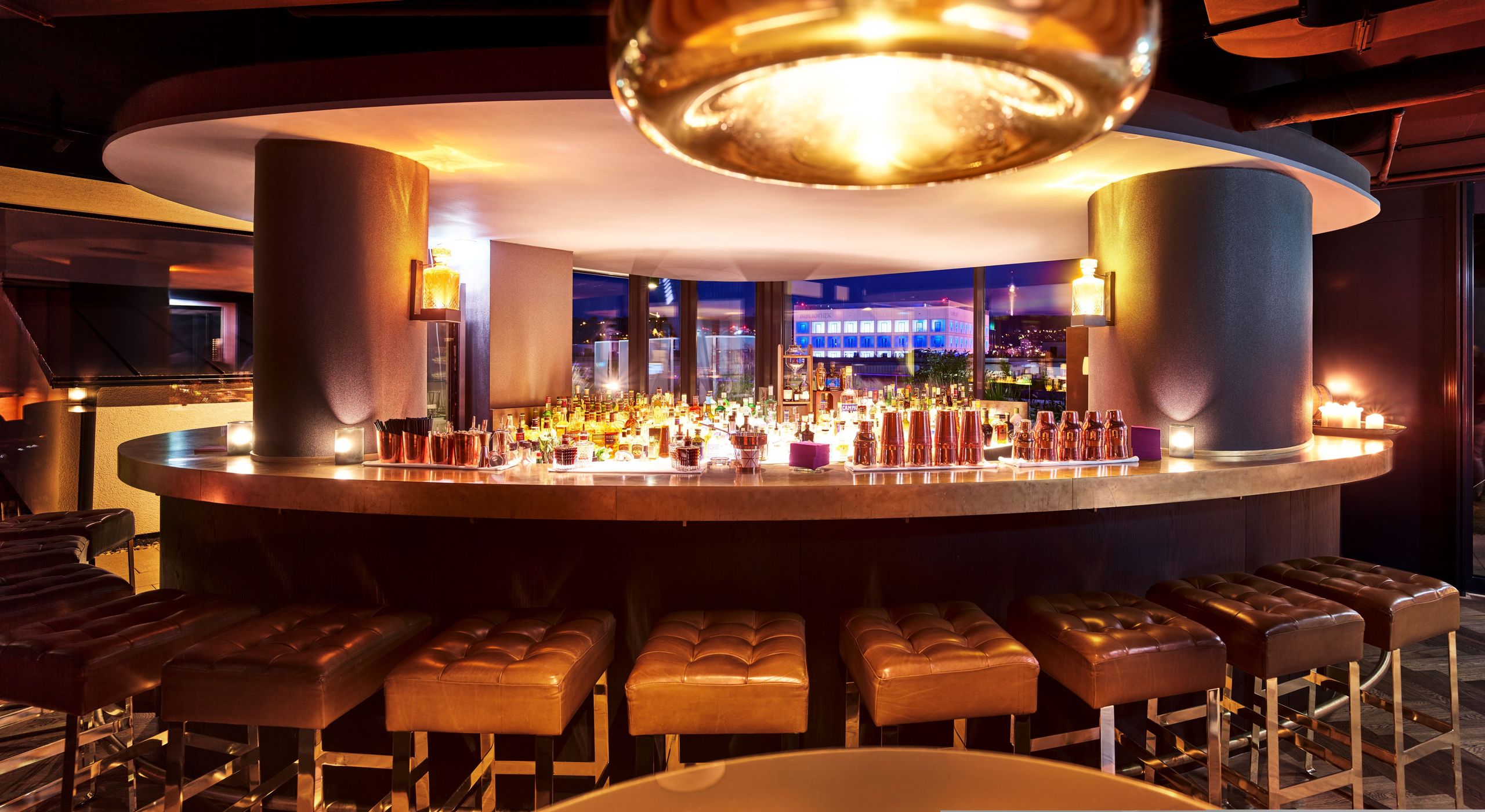 Eine moderne Bar mit Hockern, die um einen gebogenen Tresen angeordnet sind, beleuchtet von warmem…