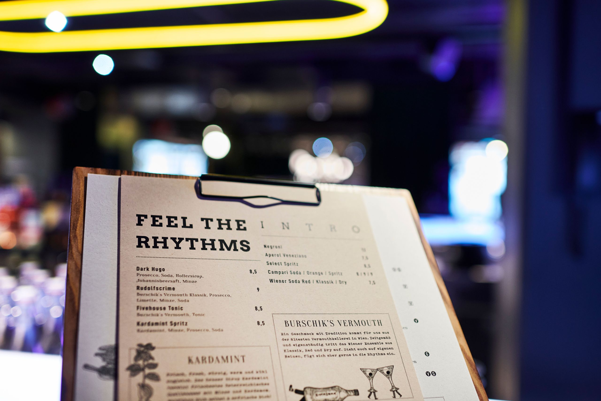 A close-up of a menu on a clipboard in a dimly lit restaurant or bar.