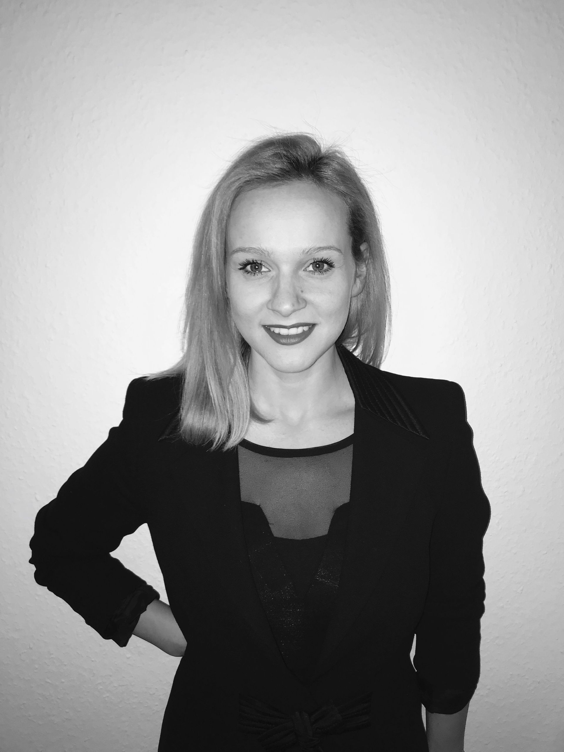 A black-and-white portrait of a smiling woman with shoulder-length hair, wearing a dark jacket…