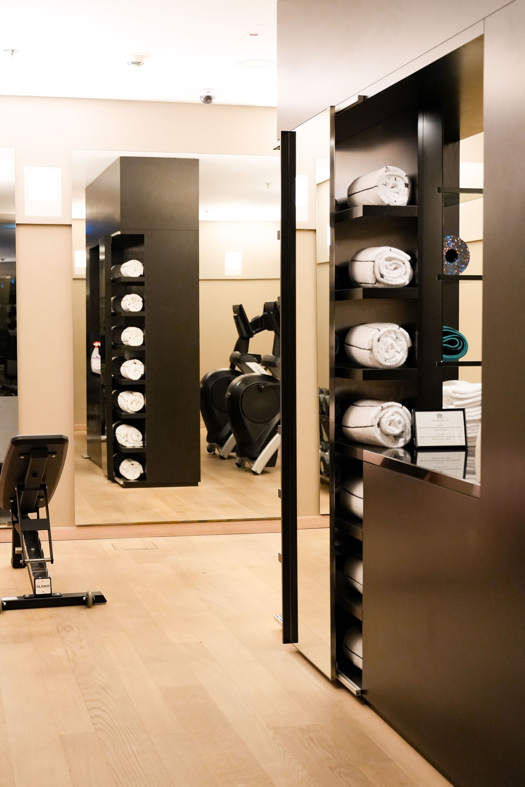 Das Foto zeigt einen Fitnessbereich mit Trainingsgeräten und Regalen mit aufgerollten Handtüchern.