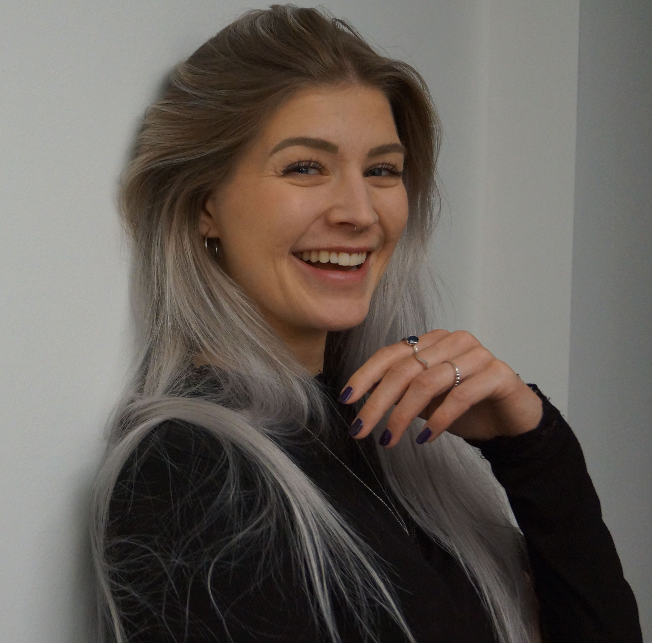 A smiling woman with long light-colored hair wearing a dark top.