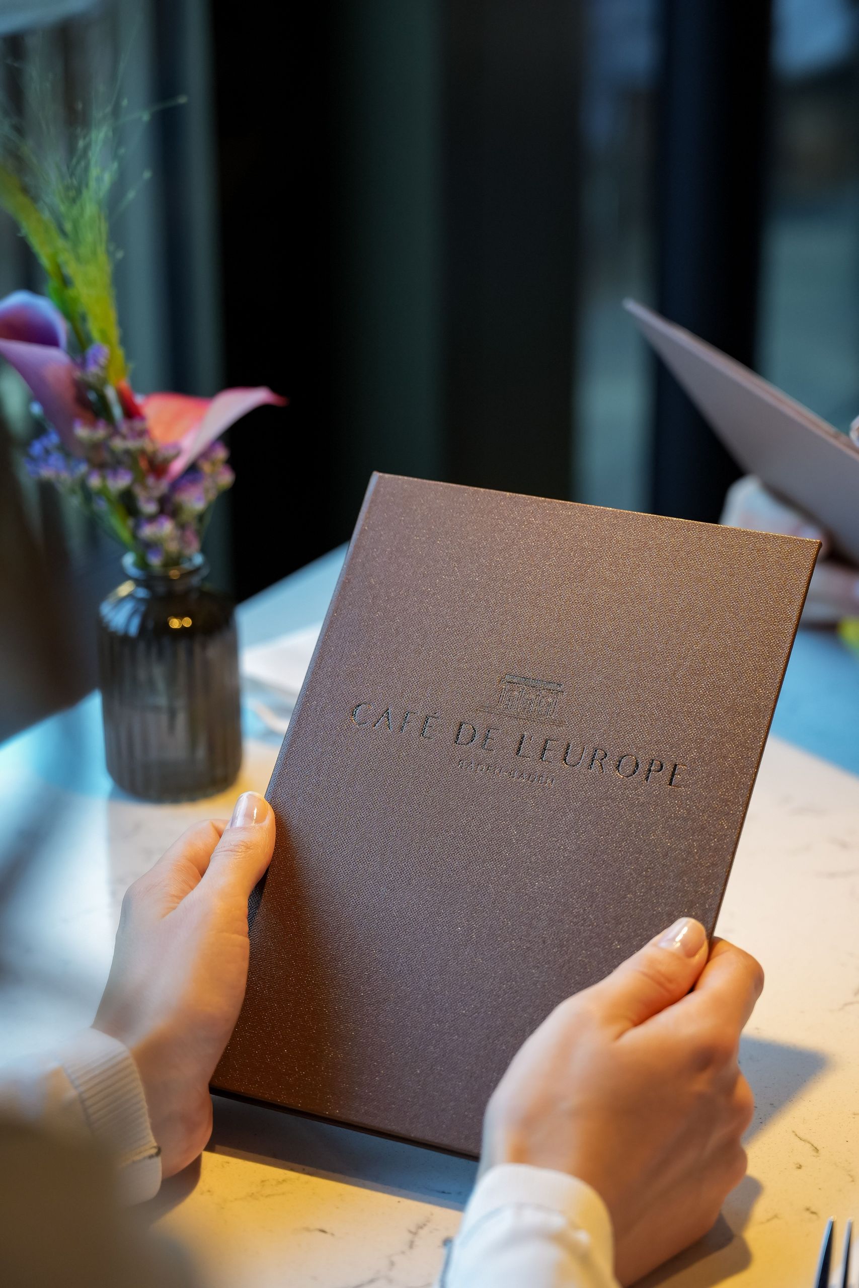 Eine Person hält eine Speisekarte an einem Tisch in einem Restaurant.