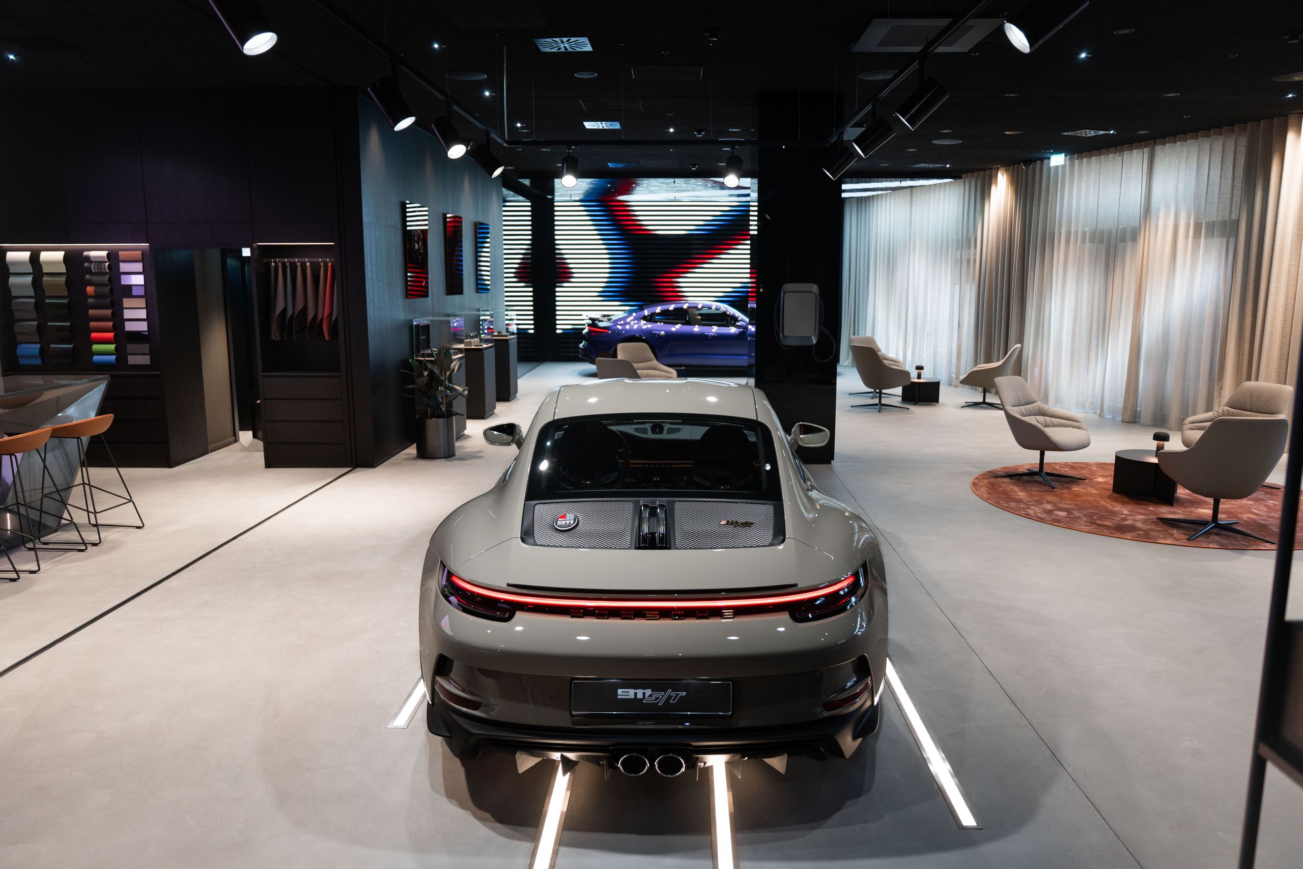 Современный автосалон с роскошным спортивным автомобилем и зоной отдыха с креслами и столами.