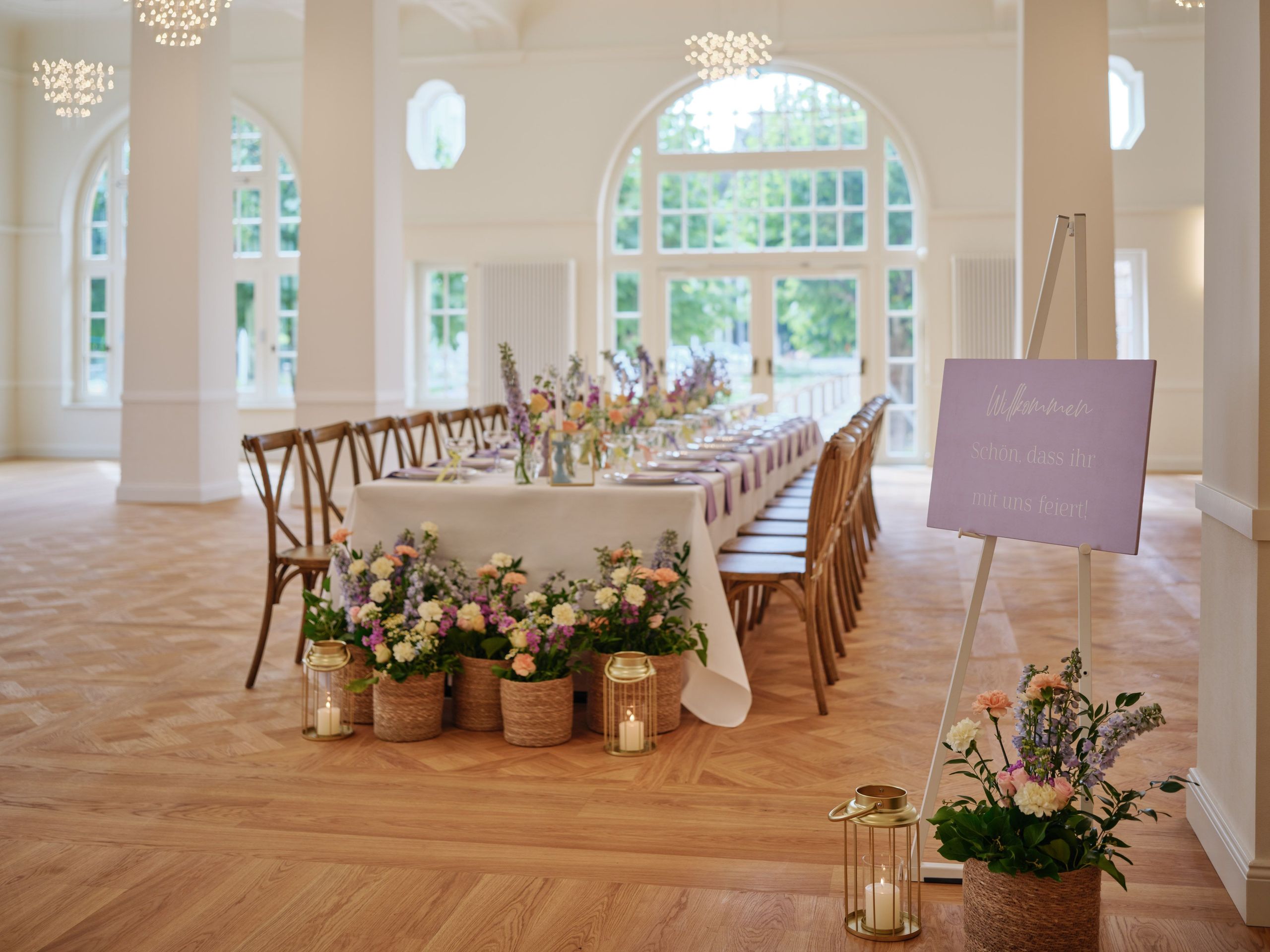 Ein langer Esstisch, der für eine Veranstaltung in einem hellen Raum mit großen Fenstern gedeckt…