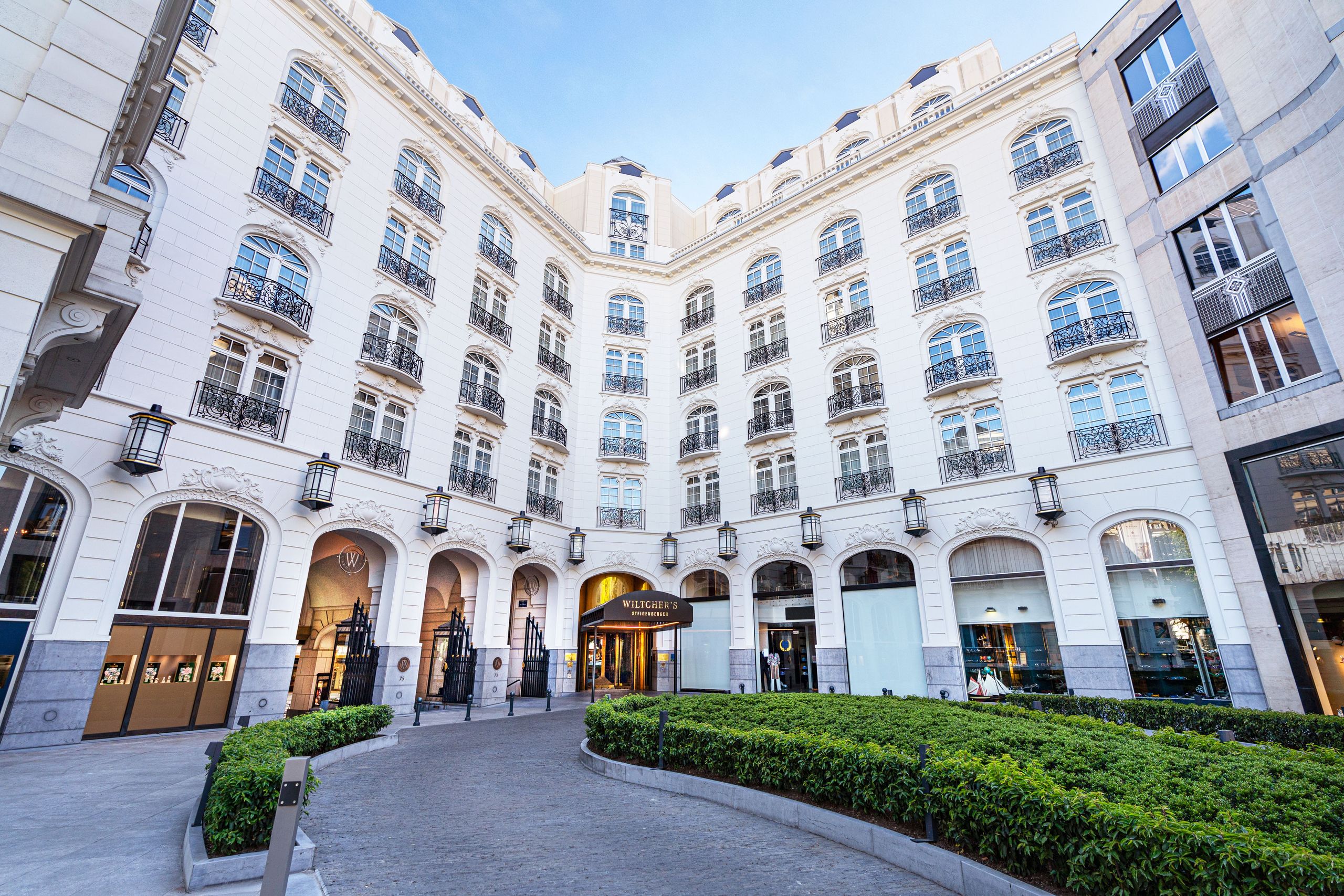 La foto muestra el exterior de un edificio blanco de varios pisos con varias ventanas y balcones…