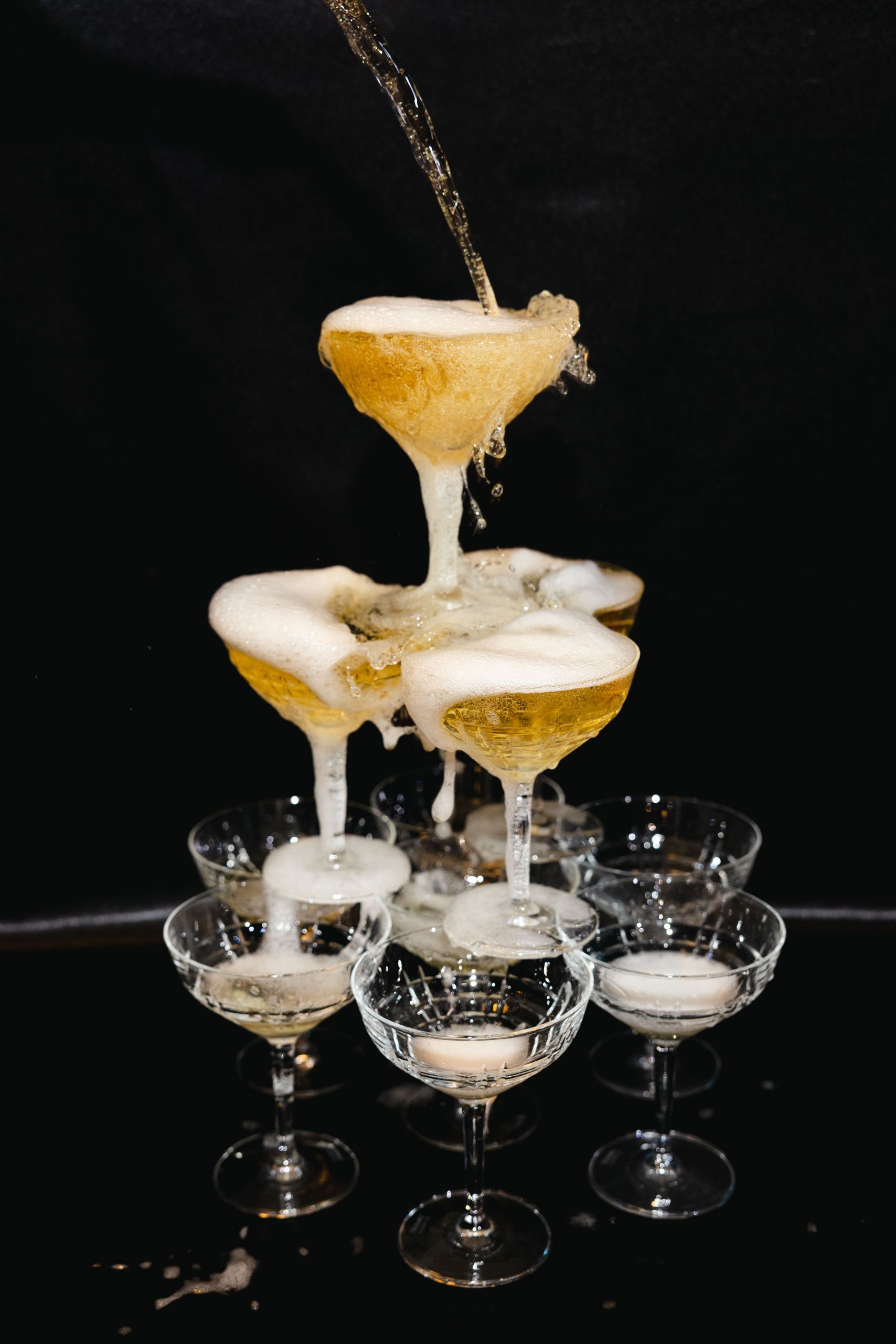 Ein Champagner-Turm wird gefüllt, wobei Bläschen überlaufen und die gestapelten Gläser hinabfließen.