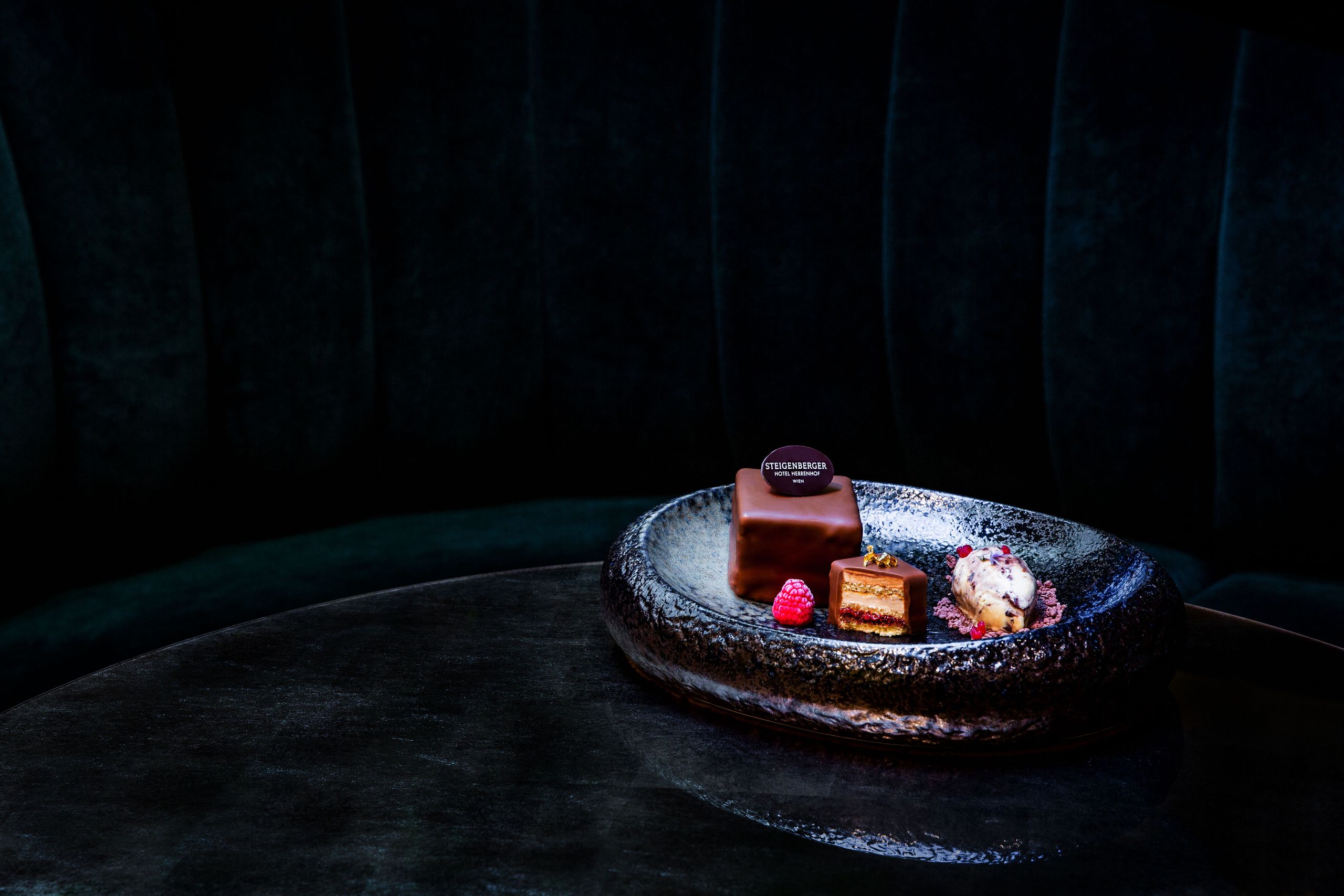 Ein Dessertteller mit einem Schokoladenkuchen, einer Kugel Eis und einer Himbeere auf einem…