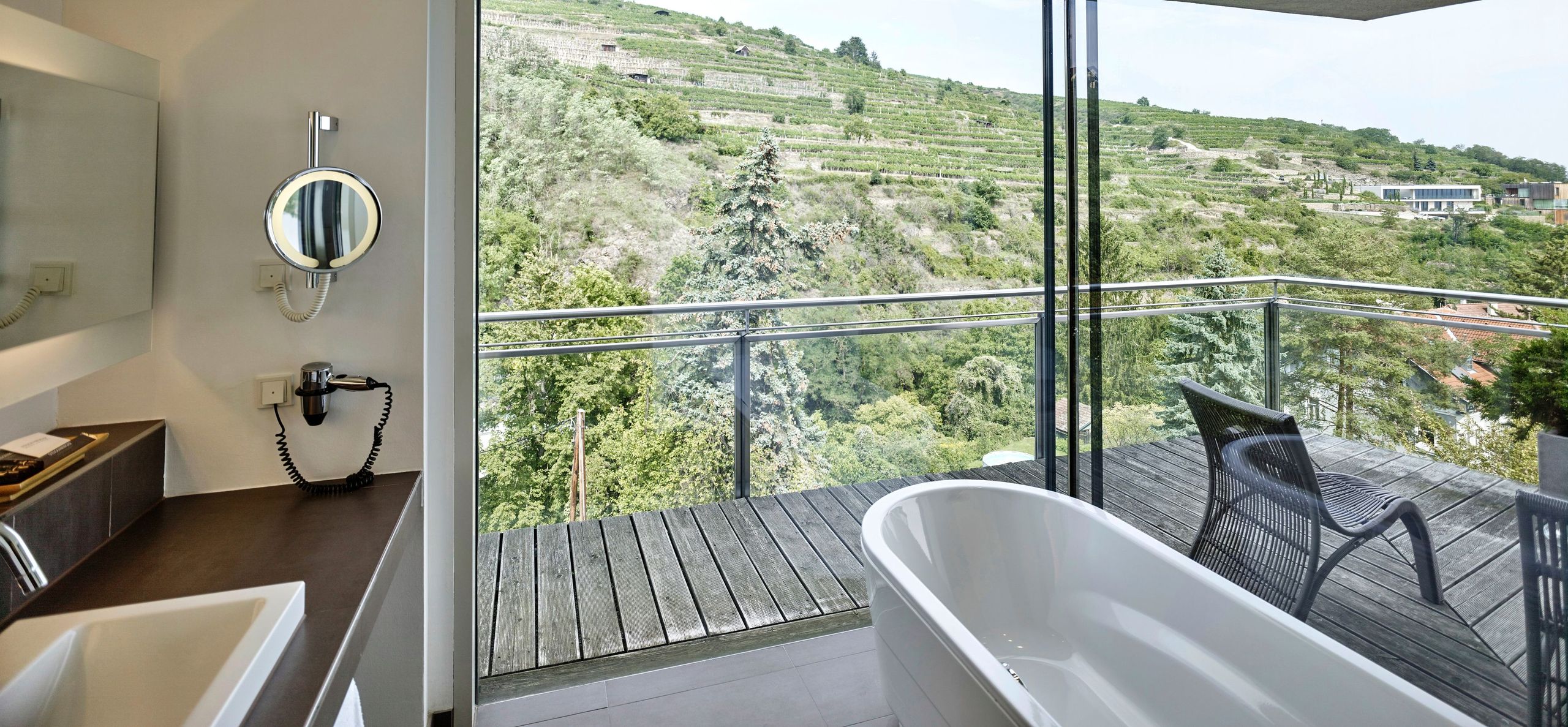 Un baño moderno con una bañera independiente y una pared de vidrio que ofrece una vista de una colina verde.