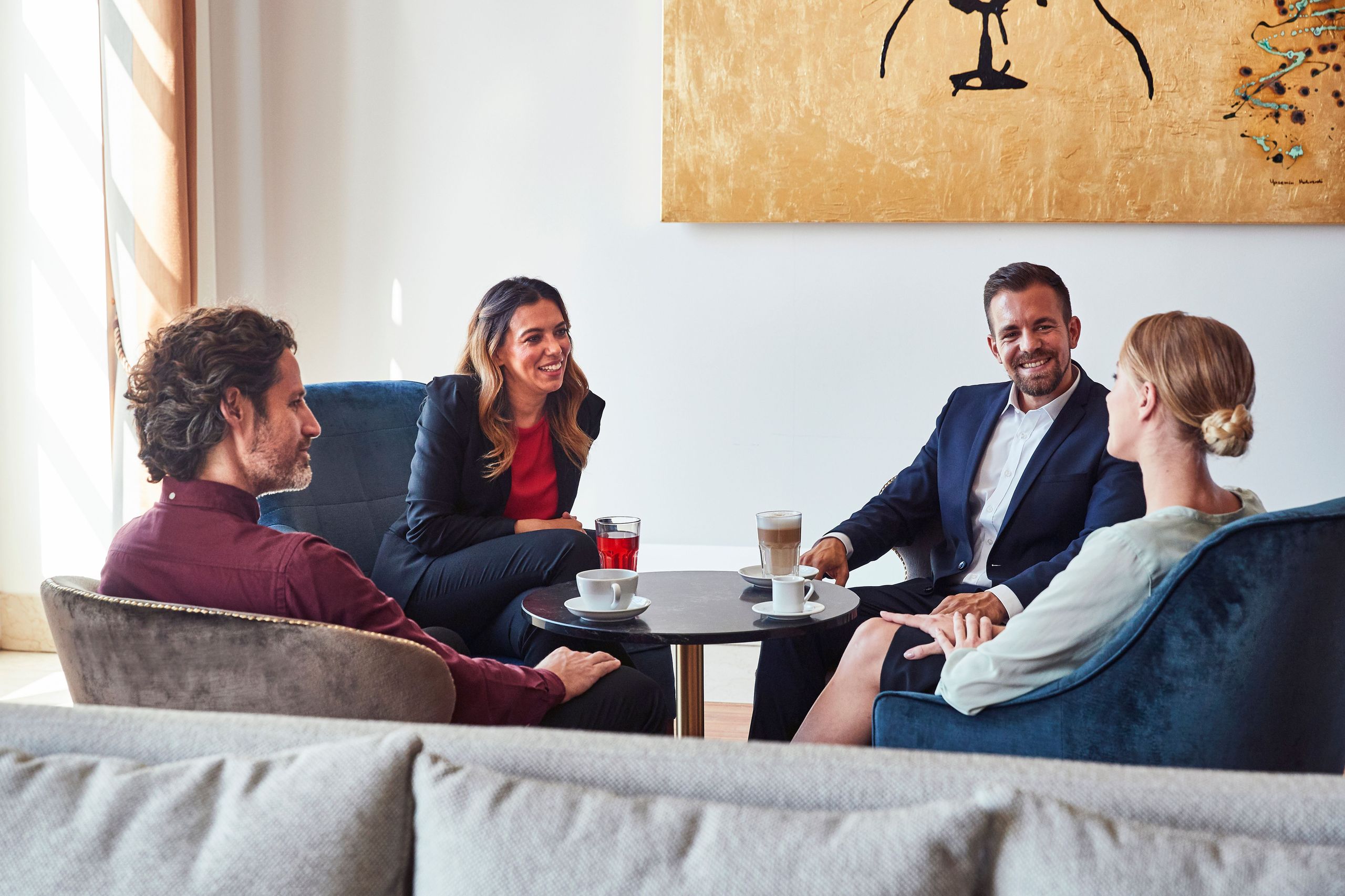 Vier Personen sitzen an einem kleinen Tisch und führen ein Gespräch in einer ungezwungenen Umgebung.