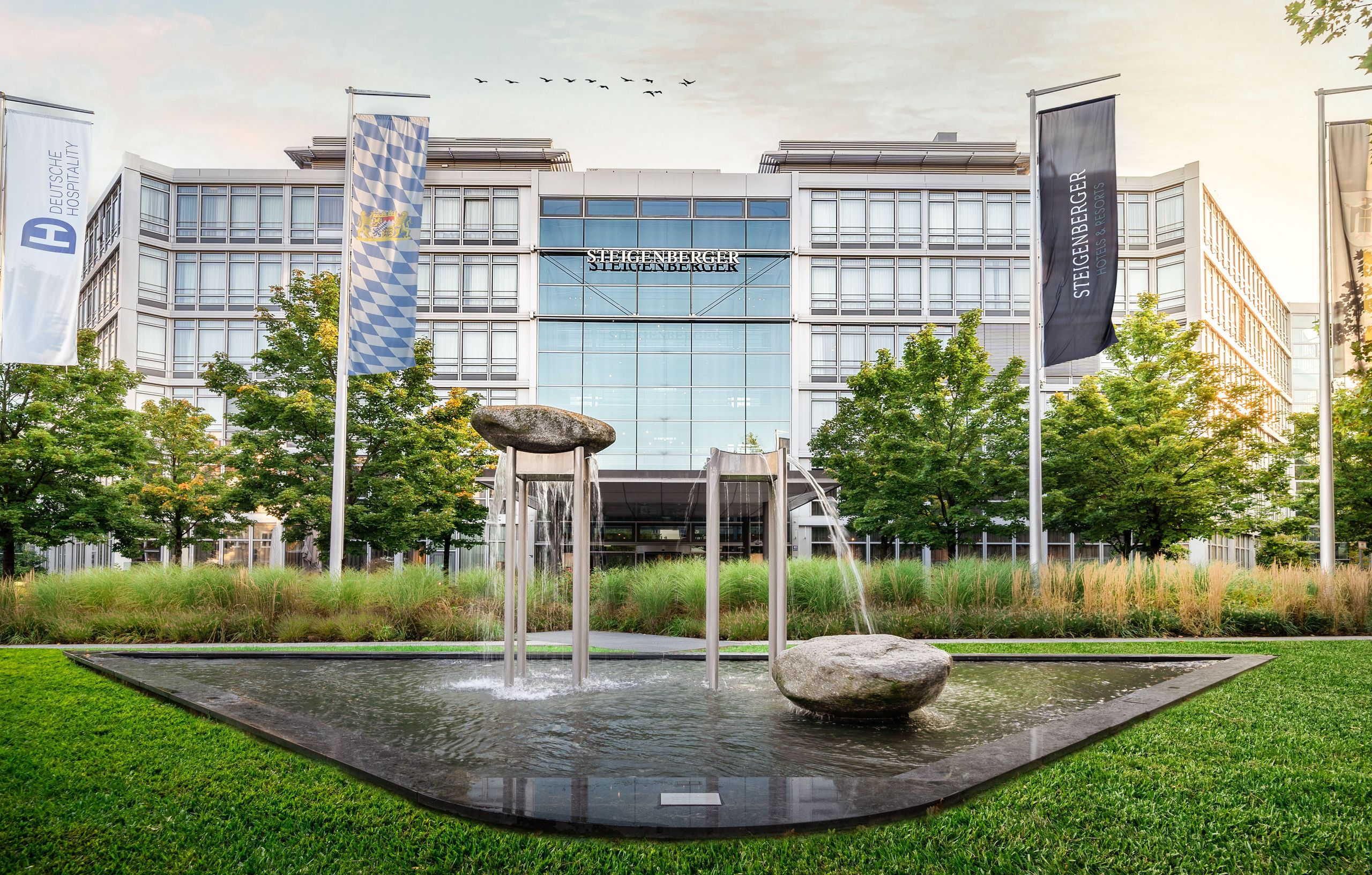 Un bâtiment de bureaux moderne avec une fontaine d'eau et des drapeaux devant.