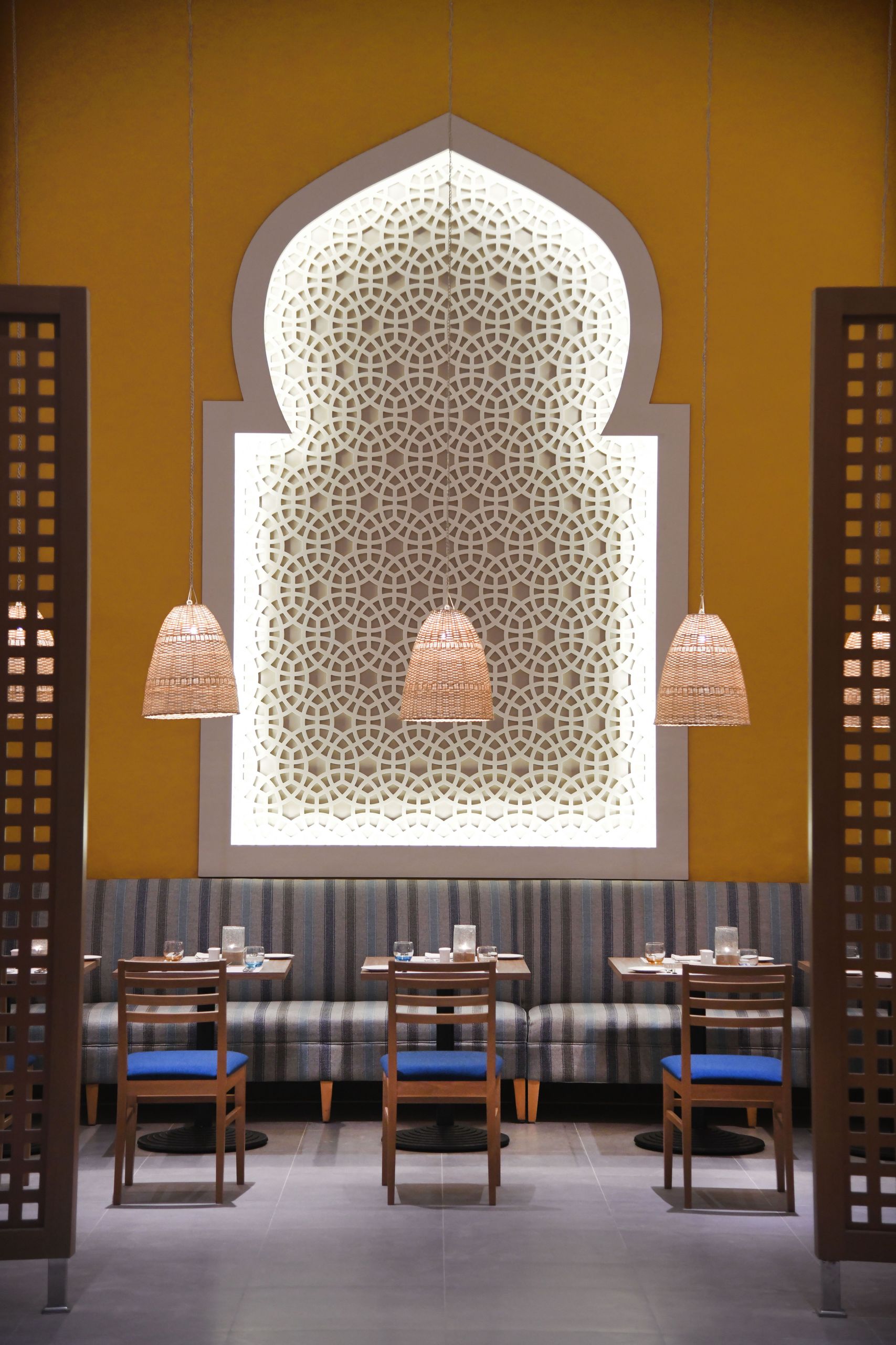 تُظهر الصورة داخل مطعم مع لوحة حائط زخرفية، وأضواء معلقة، وطاولات طعام مع كراسي.