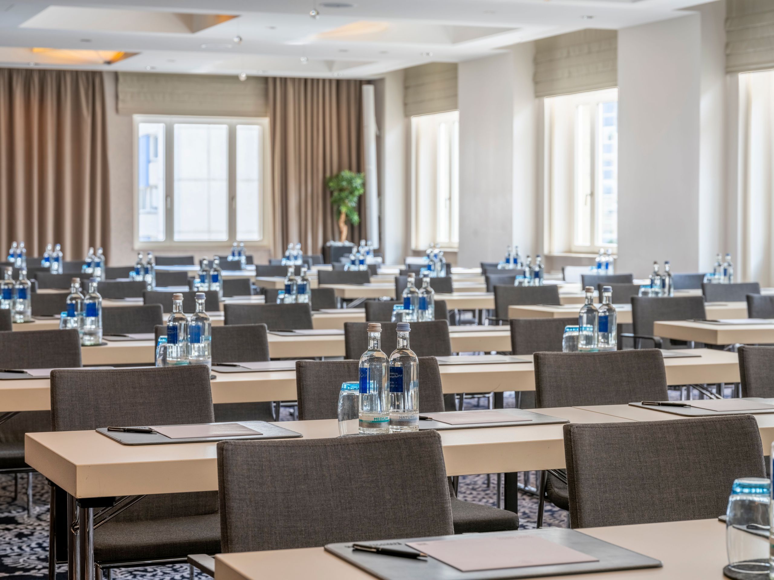 Ein Konferenzraum mit Reihen von Tischen und Stühlen, auf jedem Tisch Wasserflaschen und…