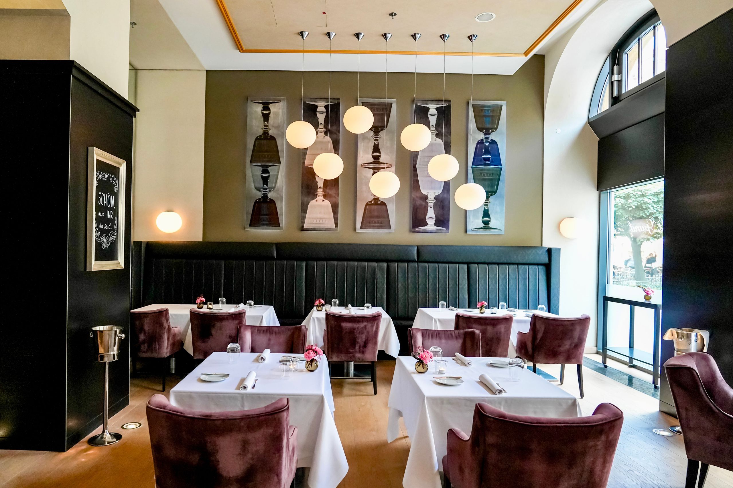 The photo shows an elegant dining area in a restaurant with tables covered in white tablecloths,…