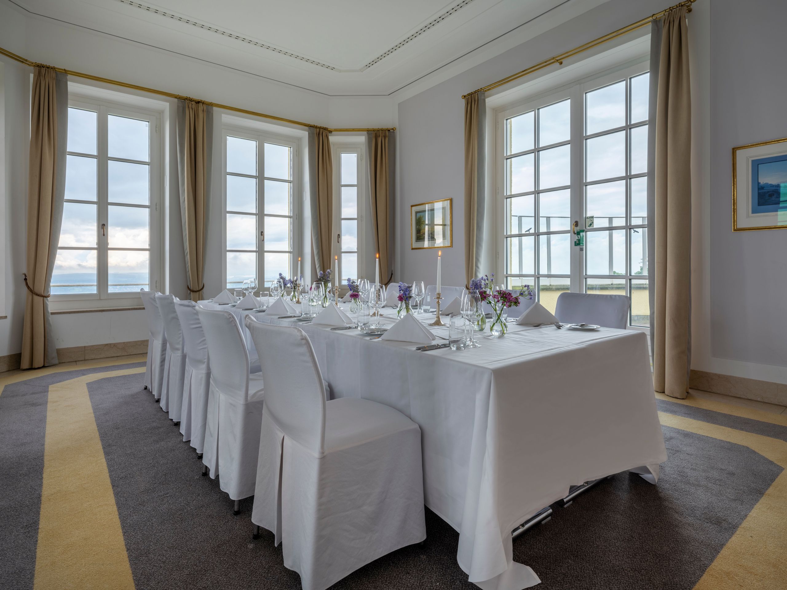 Ein Speisezimmer mit einem langen, für eine Mahlzeit gedeckten Tisch, umgeben von Stühlen und…