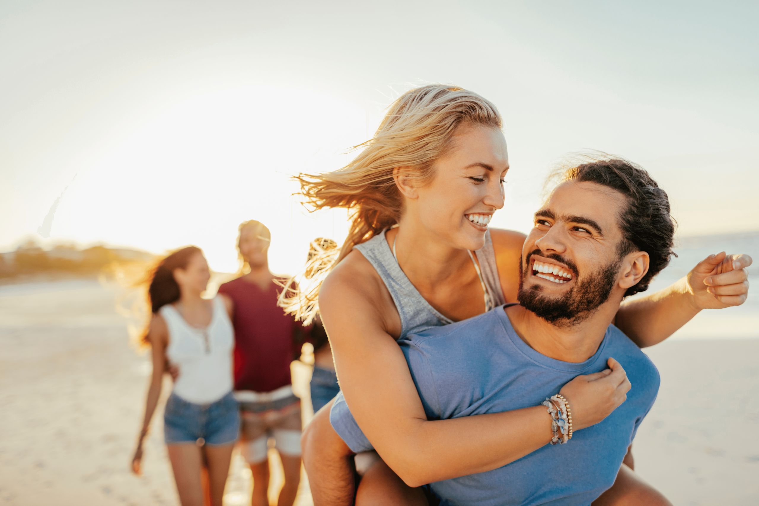 Deux couples passent du temps ensemble sur une plage, une femme donnant un tour de dos à un homme…